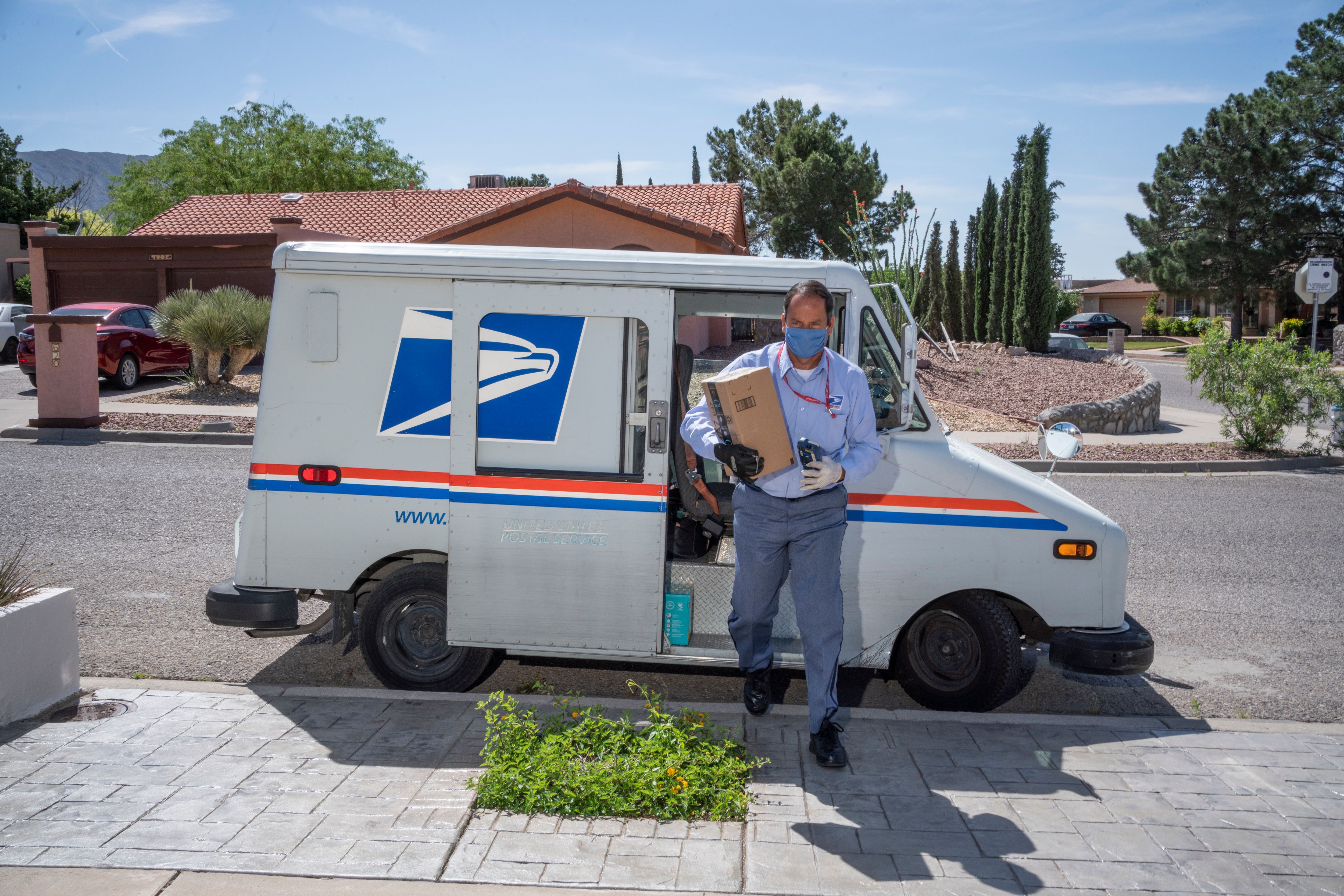 A postal employee carrying a package from their van.