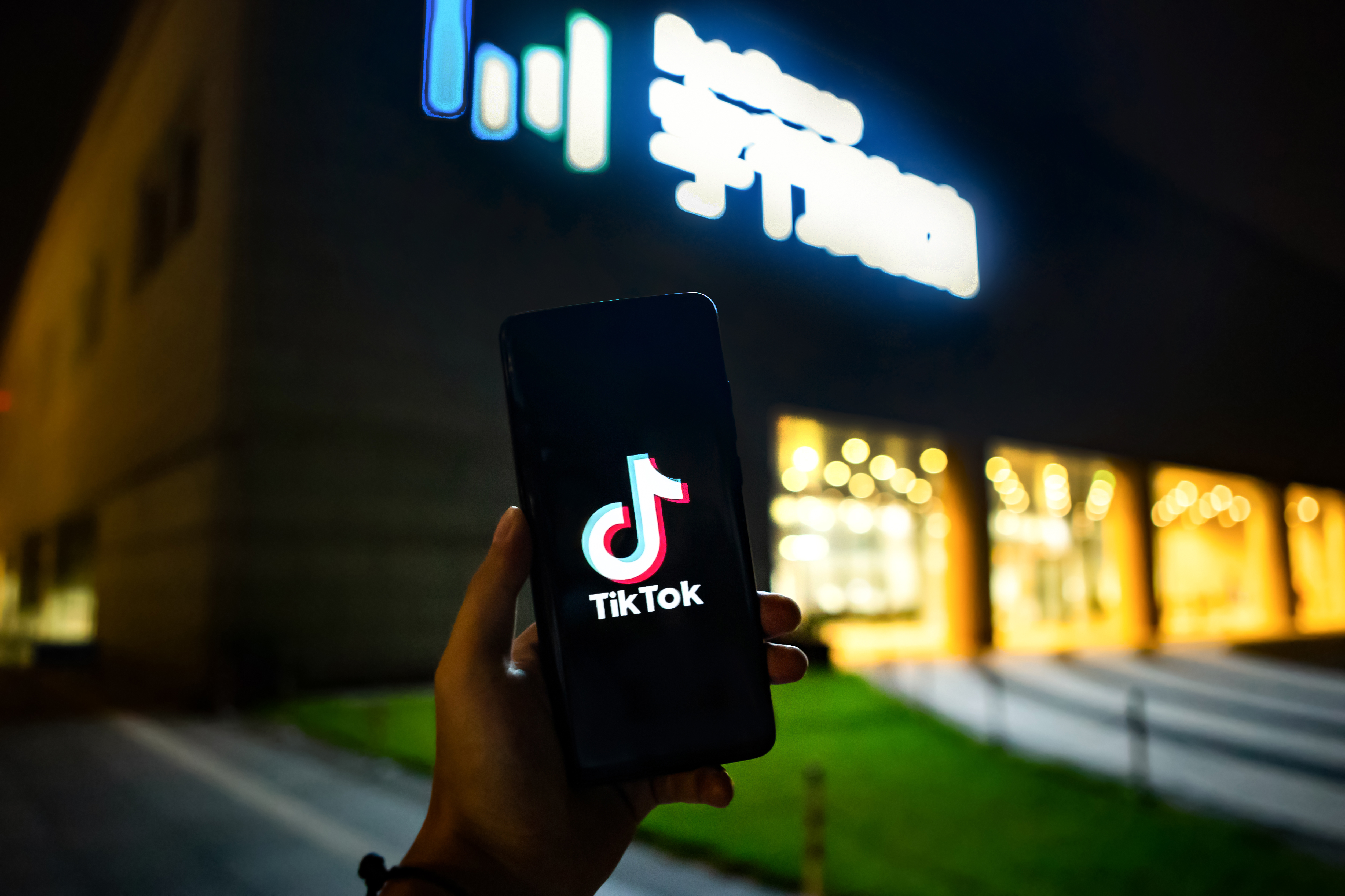 A hand holds up a phone displaying the TikTok logo in front of a building.