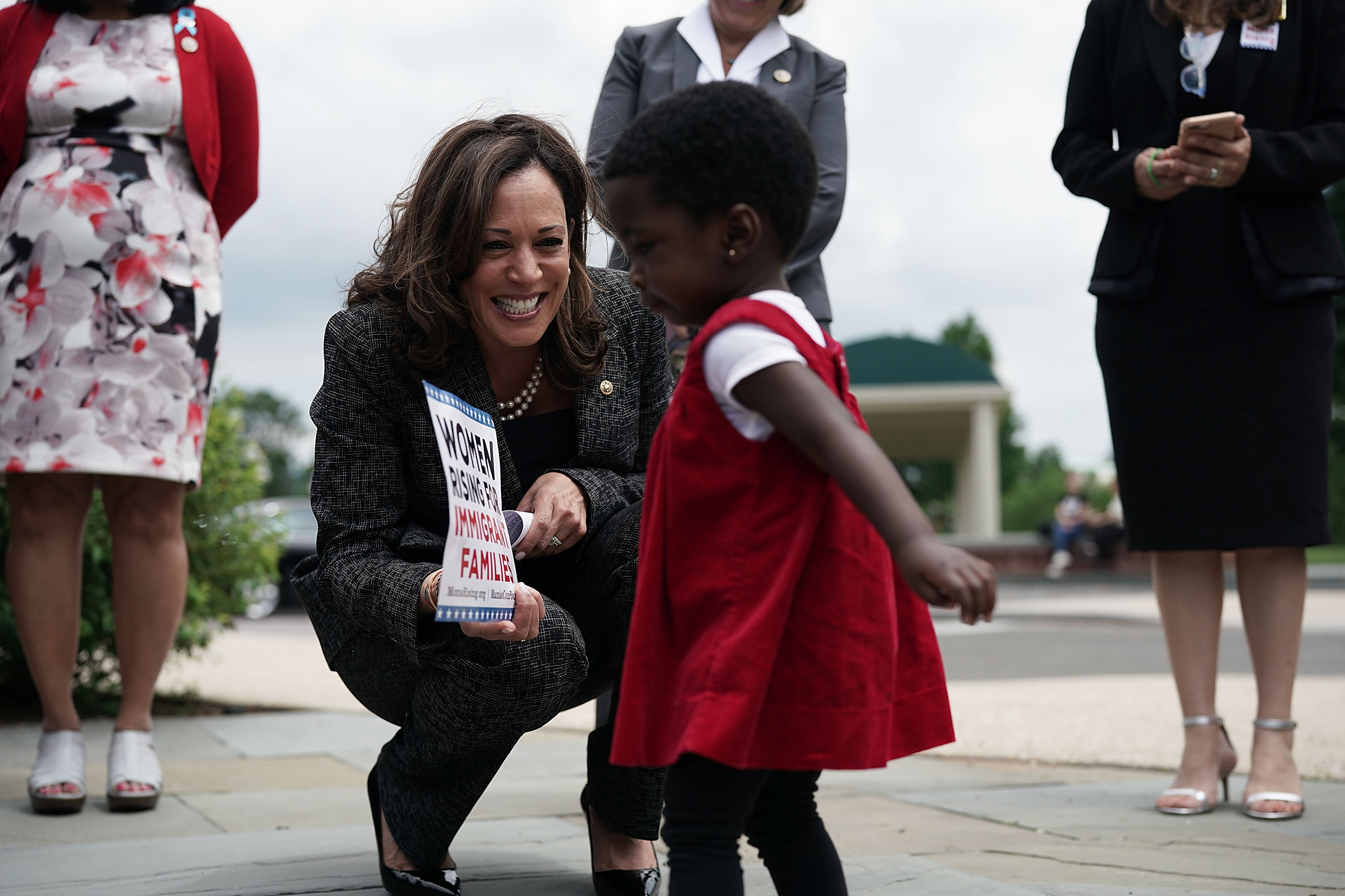 Senator Kamala Harris crouches down to smile at a toddler during a news conference.