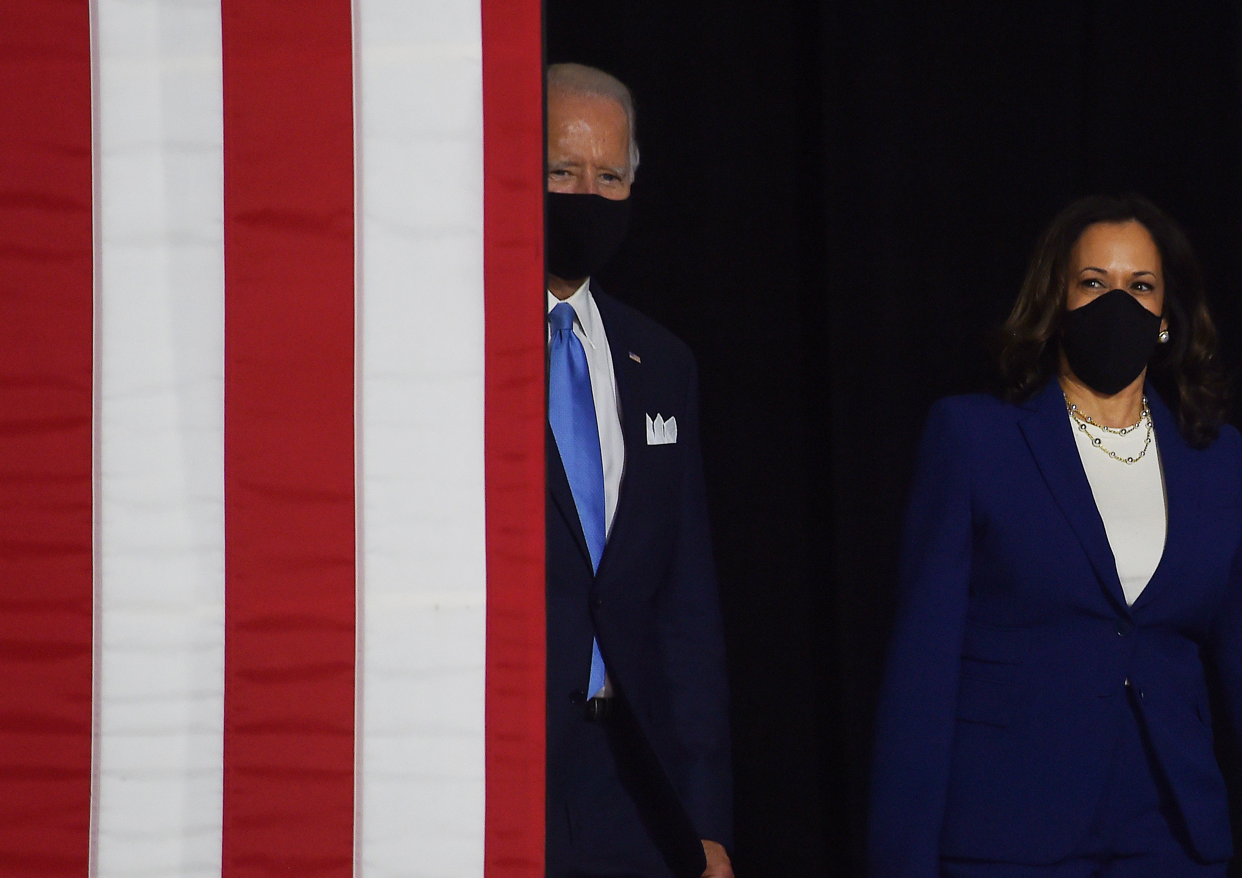 Joe Biden and Kamala Harris walking out from behind a flag-stripped banner.
