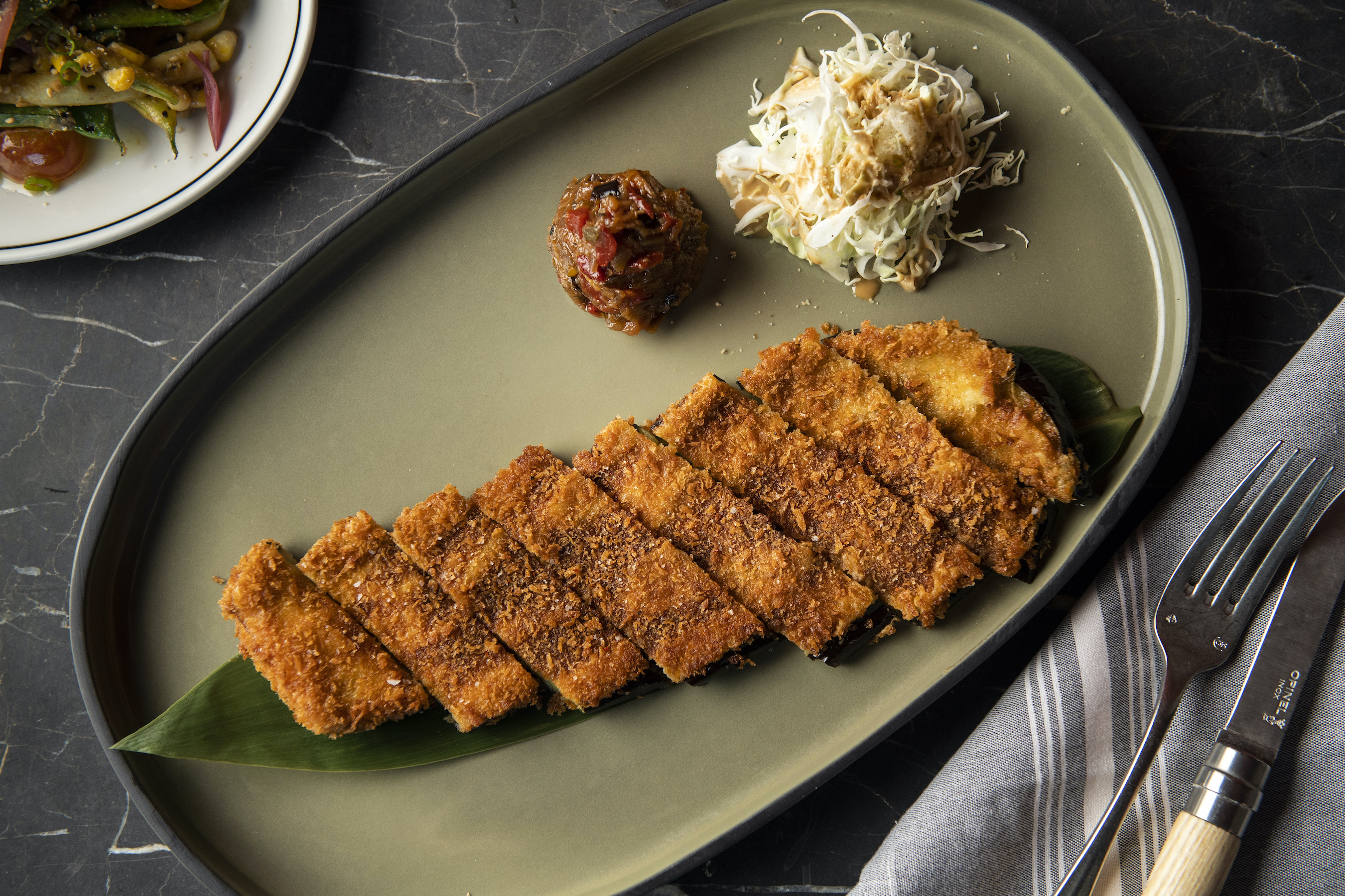 An overhead photograph of breaded and fried eggplant, cut into pieces over banana leaf