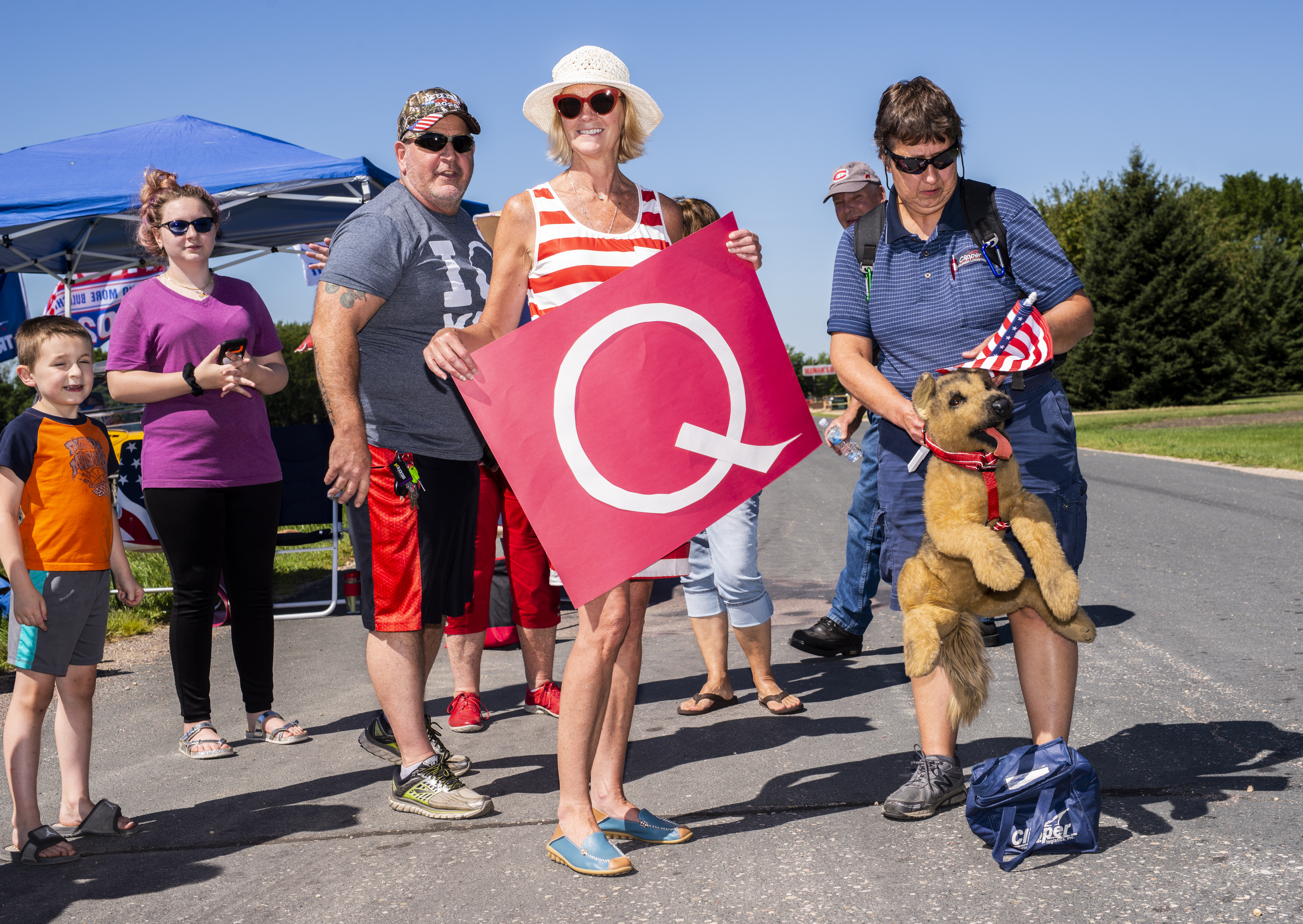 A person holding a sign with a large letter Q stands with a group of people at a roadside.