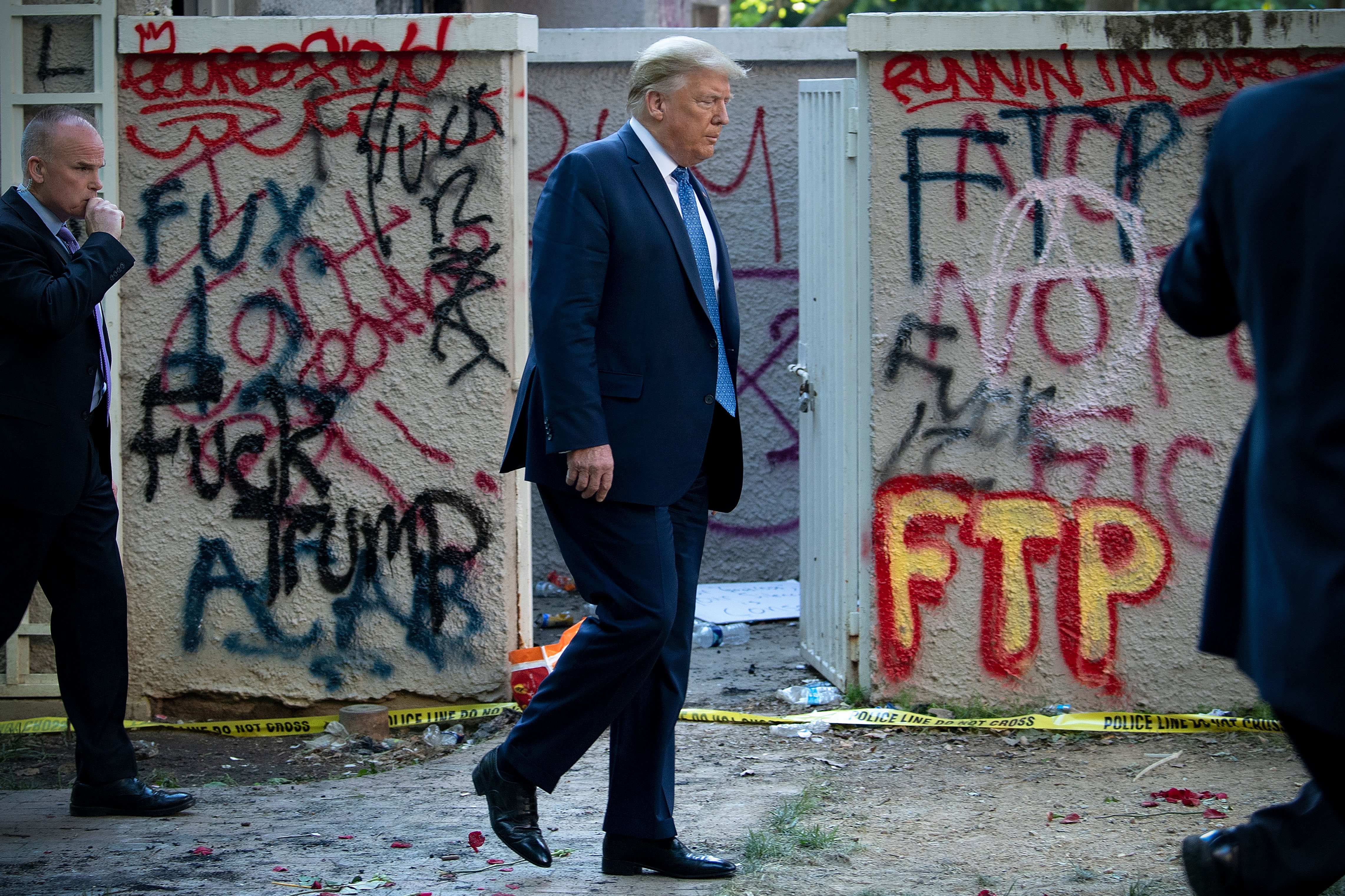 Donald Trump walking past graffitied concrete walls.