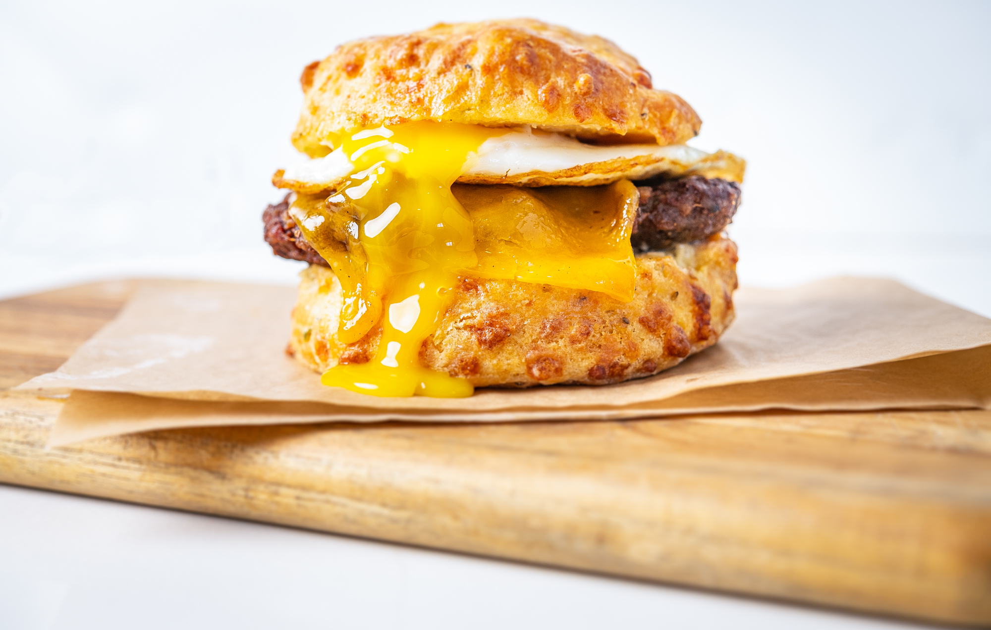 An egg sandwich with sausage oozes yolk onto a cheesy biscuit by Ghost Dog Egg Man