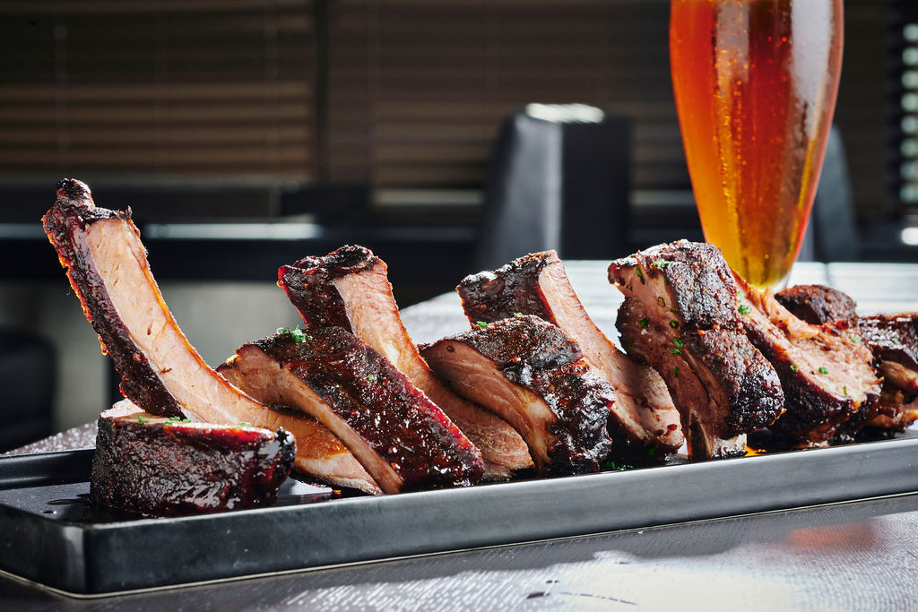 A plate of barbecue ribs and a pilsner glass full of beer.