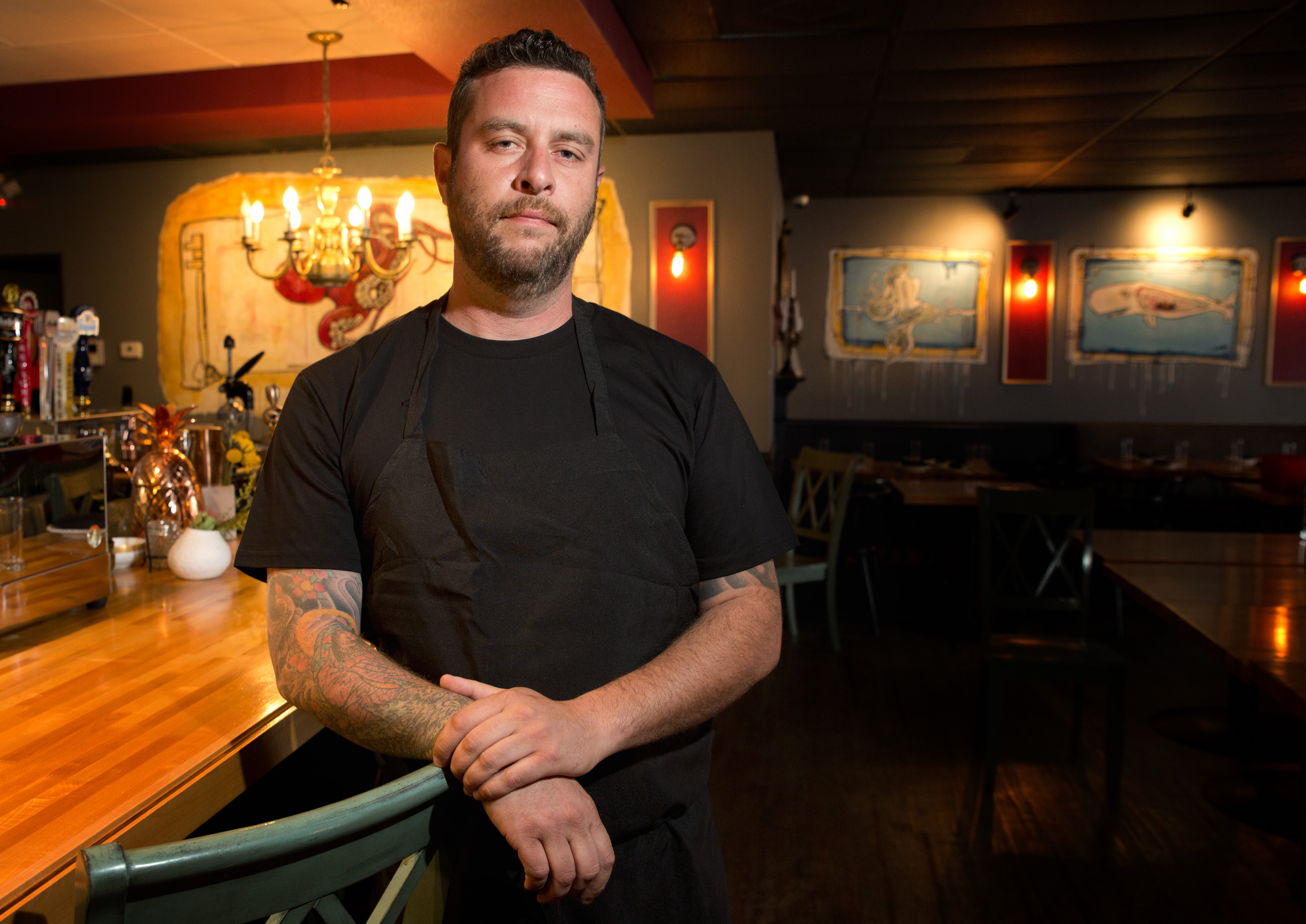A man in a black T-shirt leans against a bar
