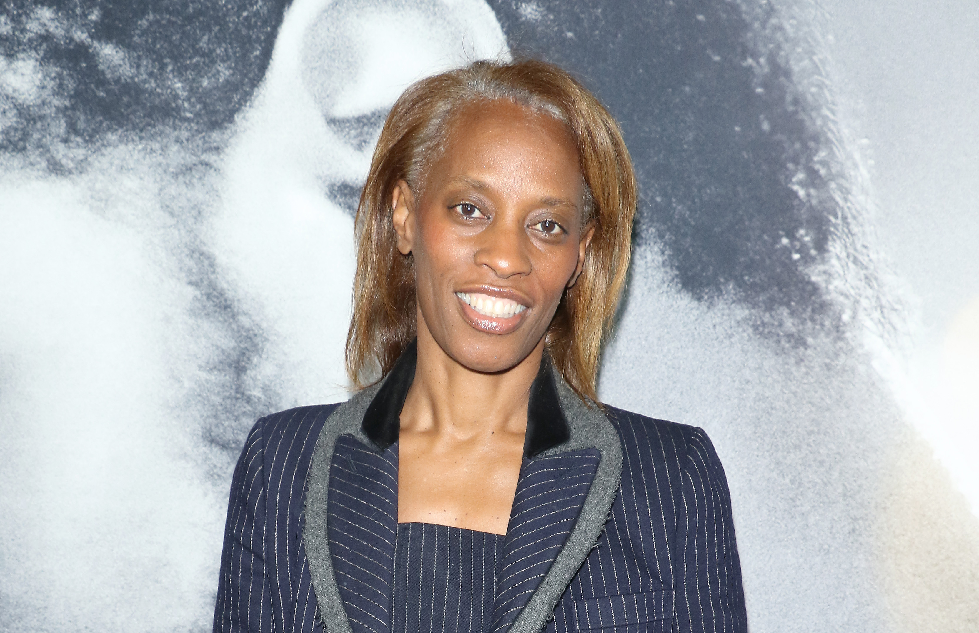 Dawn Davis, in a navy pinstripe suit, stands in front of a a large movie poster featuring LaKeith Stanfield’s ear