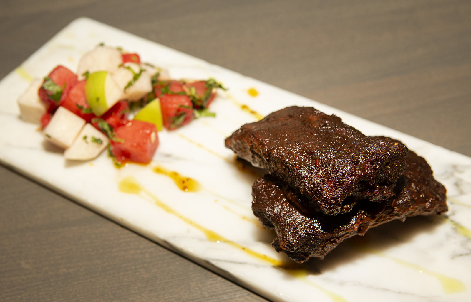 A skirt steak marinated in mole and spices on a rectangle plate with a small onion/tomato salad.