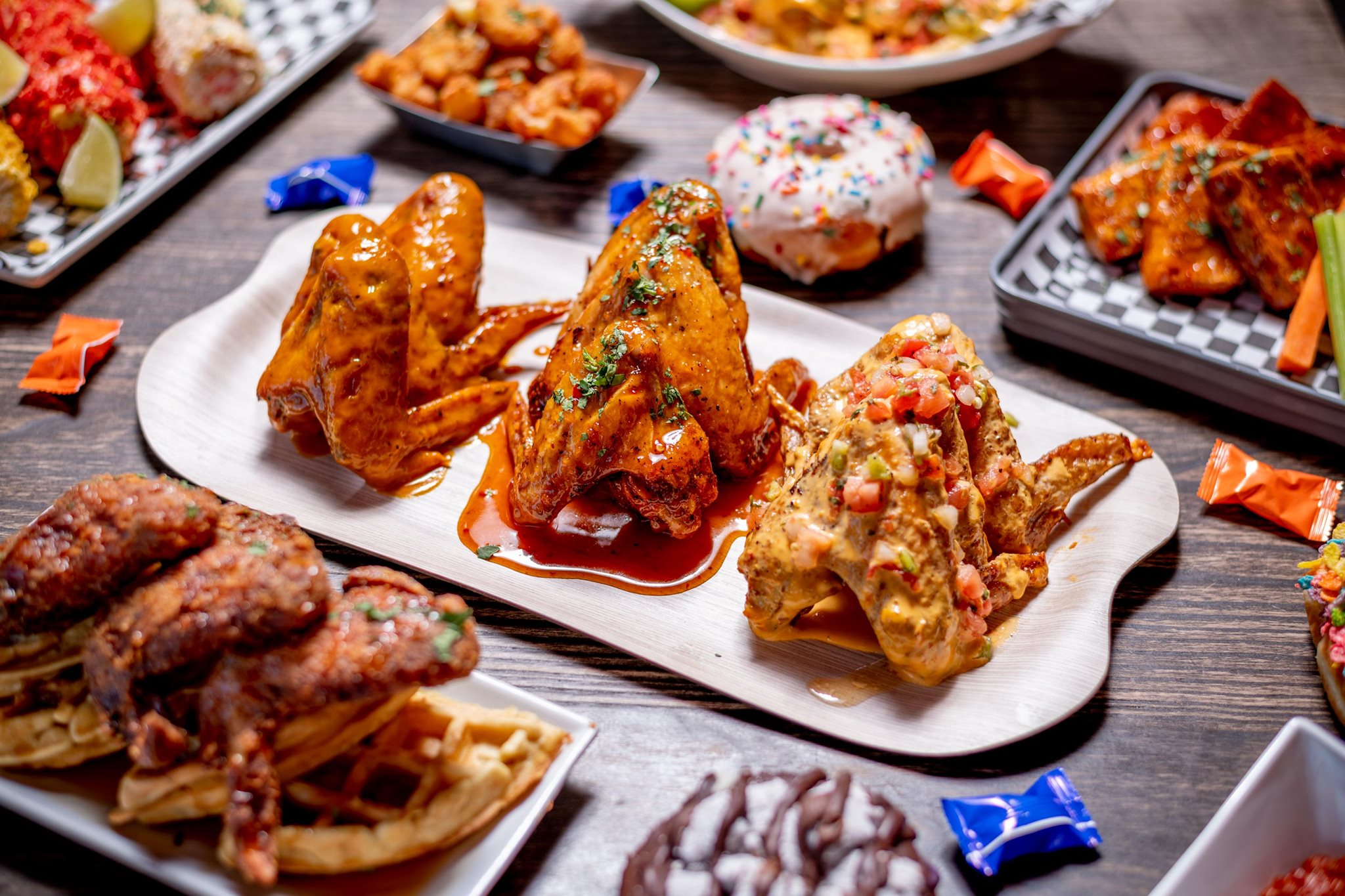 Several containers are overflowing with wings piled up and covered with different sauces. A doughnut sits in the middle of the table, a nod to the location inside Glam Doll Donuts Northeast location where B.A.D. Wingz will open