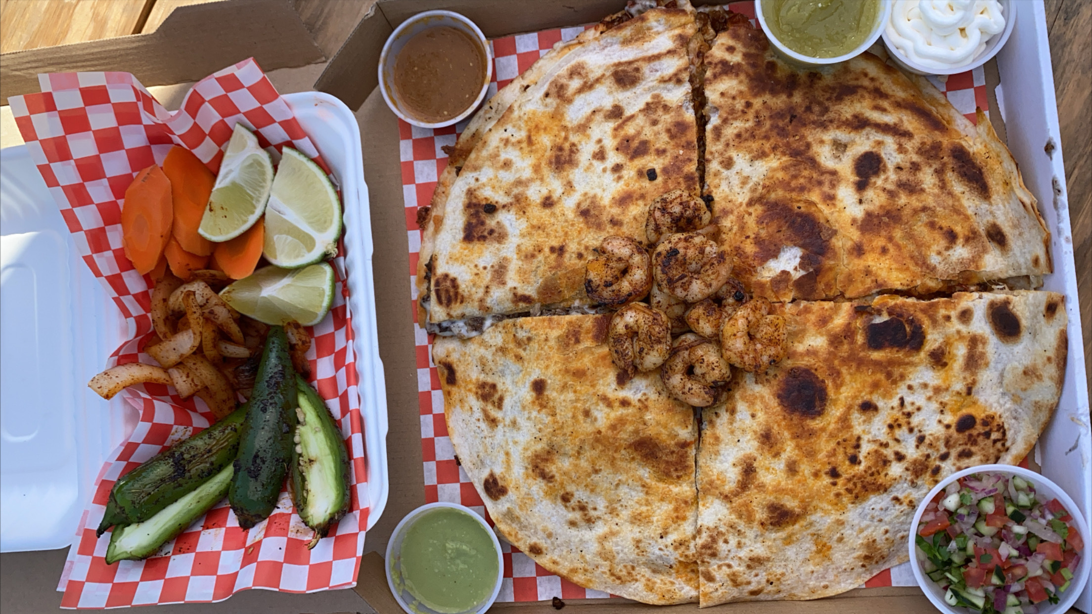 A shrimp “pizza mula”: a cheesy triple-decker quesadilla cut into quarters and served inside a pizza box, with tubs of salsa, grilled jalapenos, and limes on the side