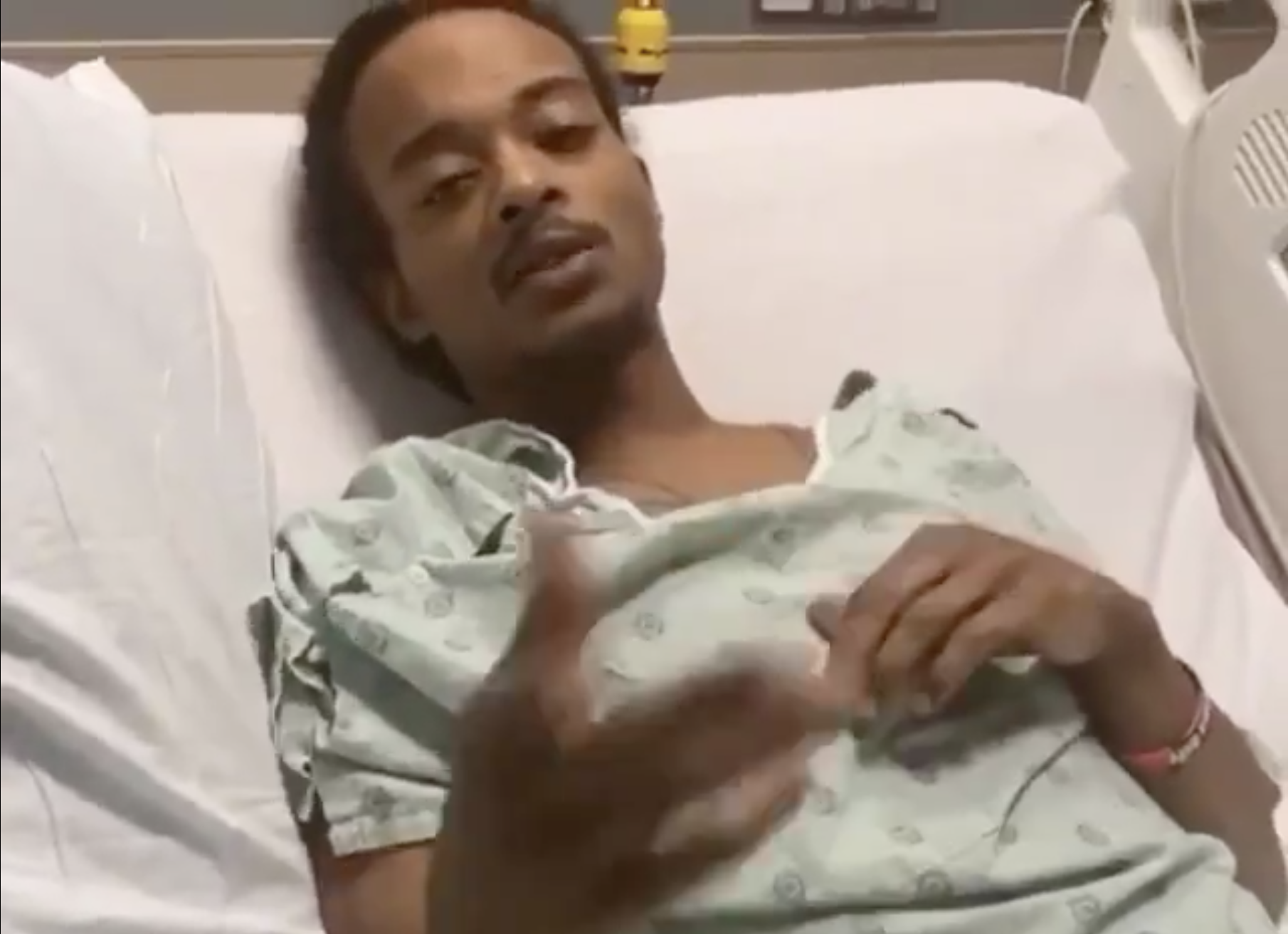 Jacob Blake, in a green hospital gown, lies in his bed, an arm extended as he gestures, speaking.