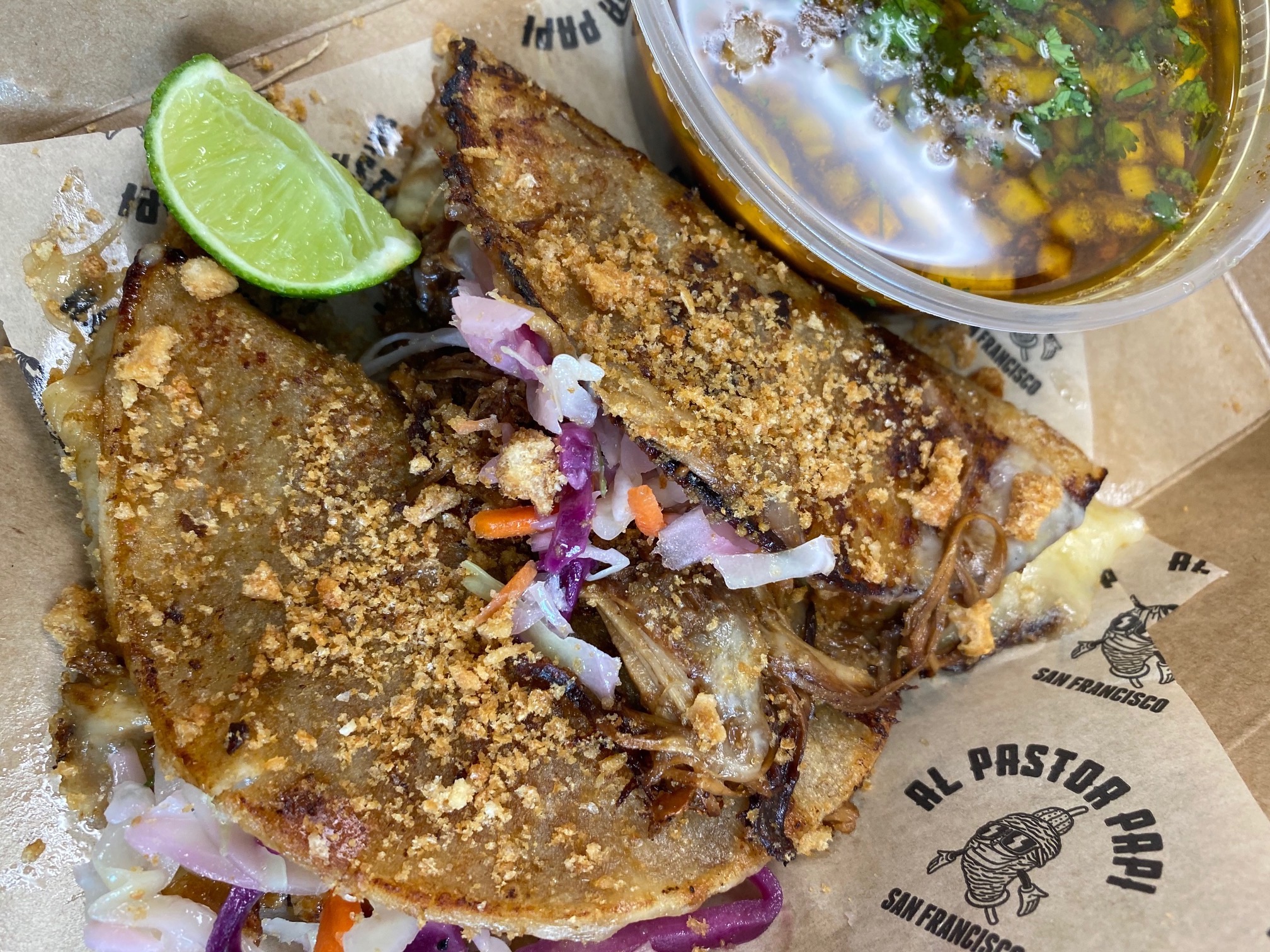 Two crispy chicken adobo tacos dusted with crushed fried pork skin, accented with a colorful cabbage slaw