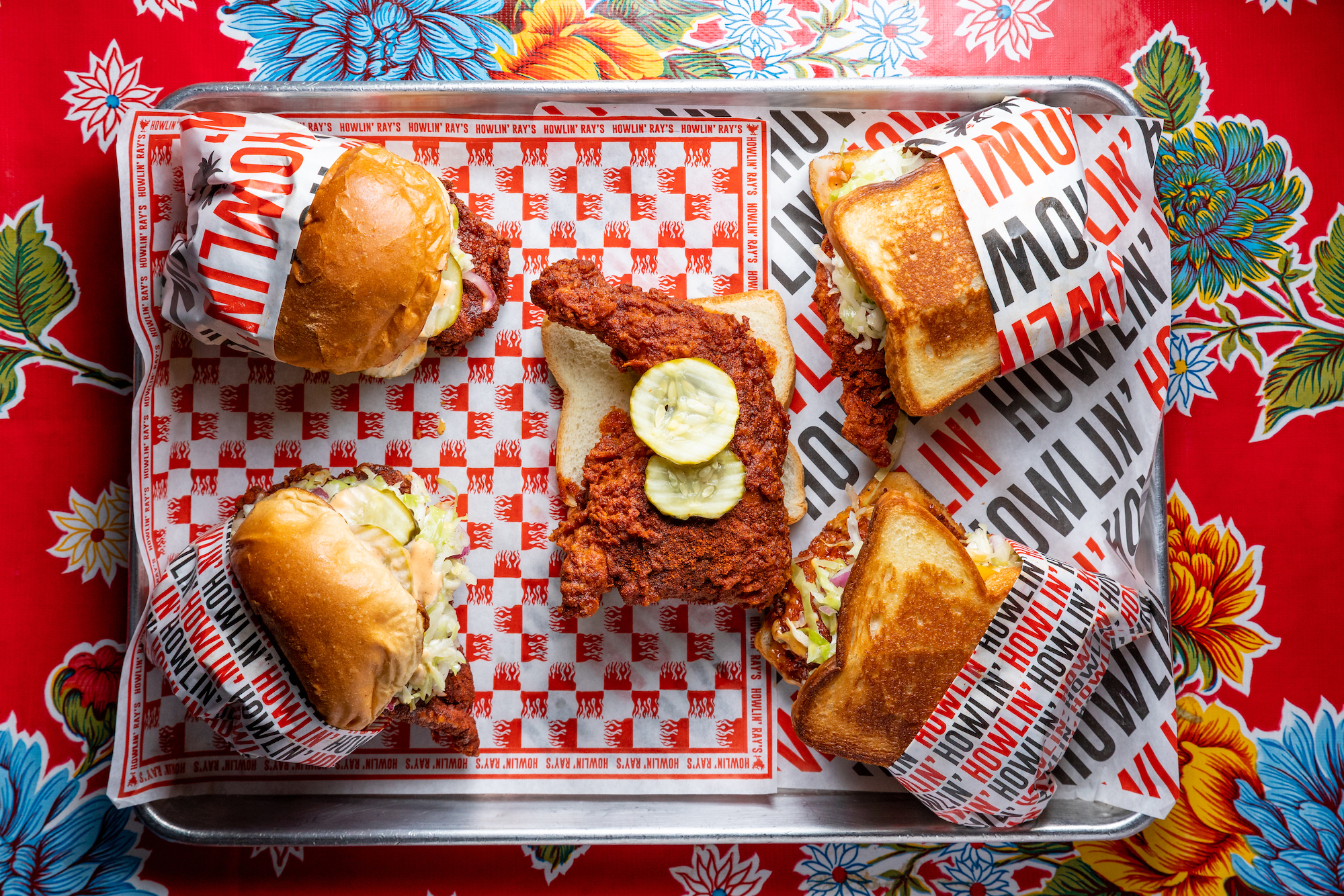 A tray of hot chicken shown from above with checkered paper beneath.