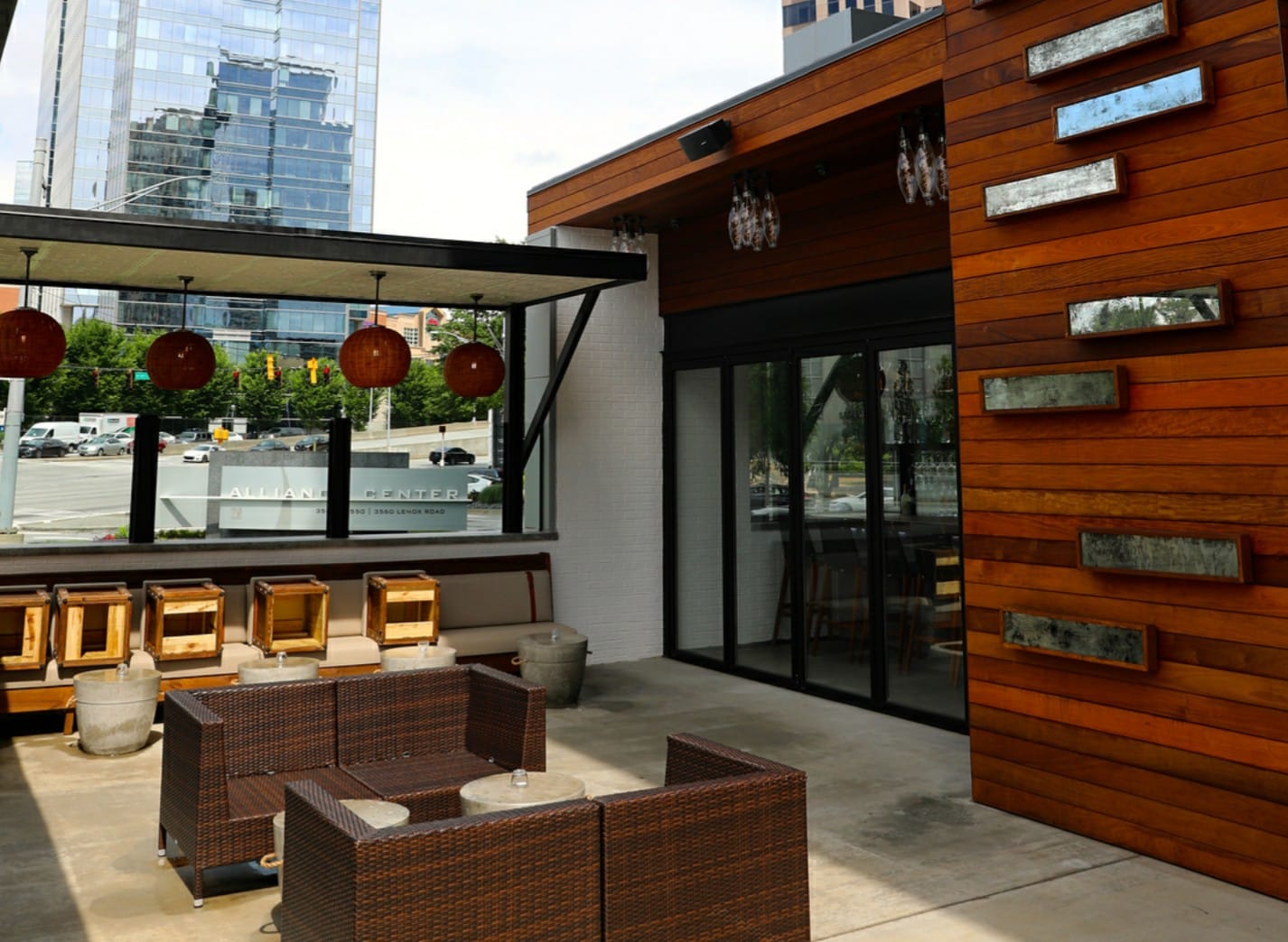 The outdoor patio with two couches, bar seating, and a wood wall with flower boxes at Little Alley Steak Buckhead, Atlanta