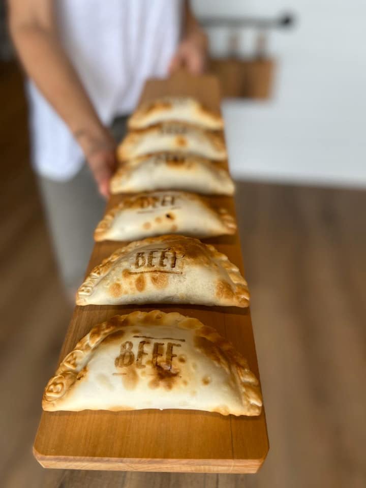 A perfectly neat row of five branded beef empanadas set upon a long, thin wooden cutting board from Belen de la Cruz in Atlanta.  