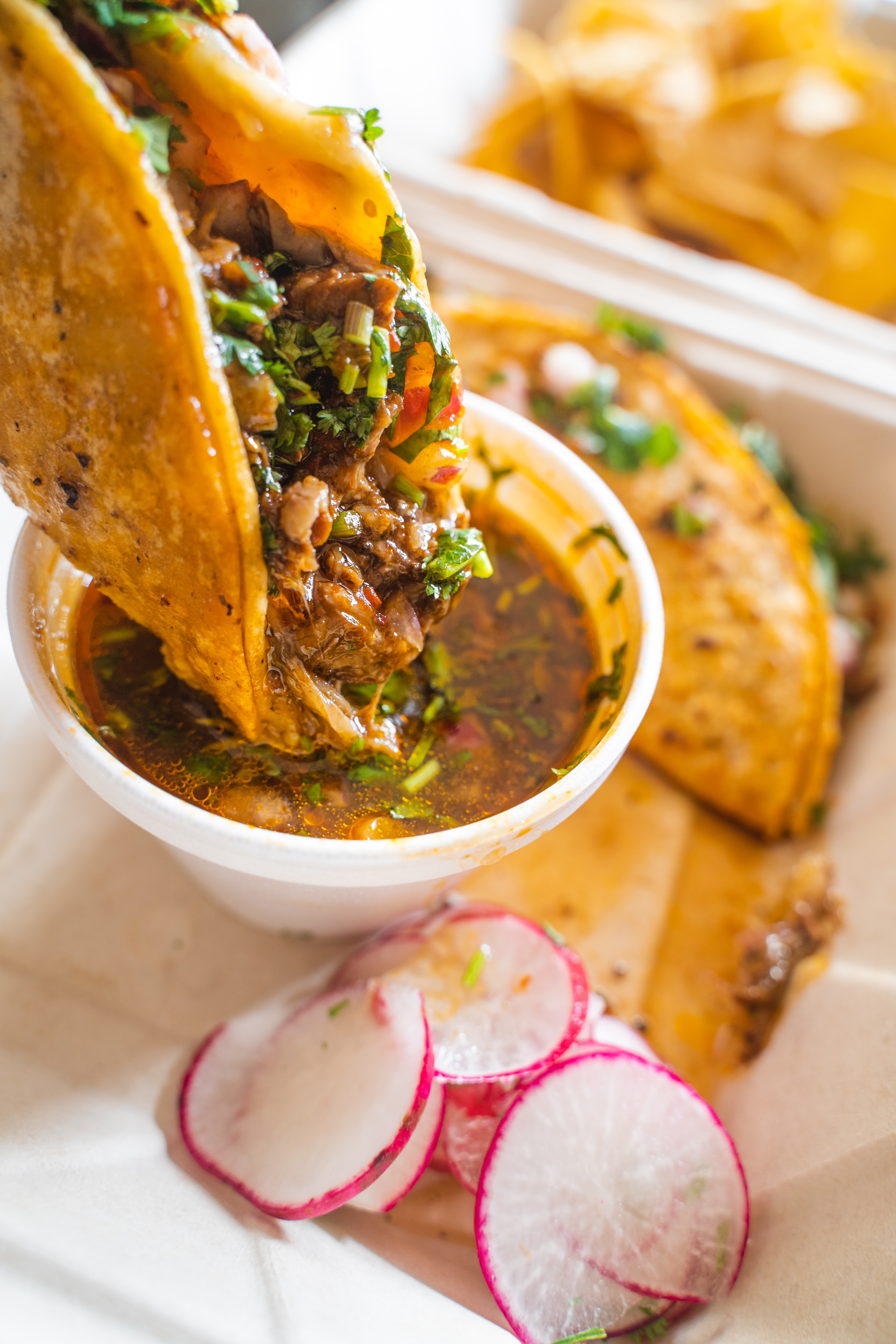 A stock photo of birria tacos being dipped into consome.