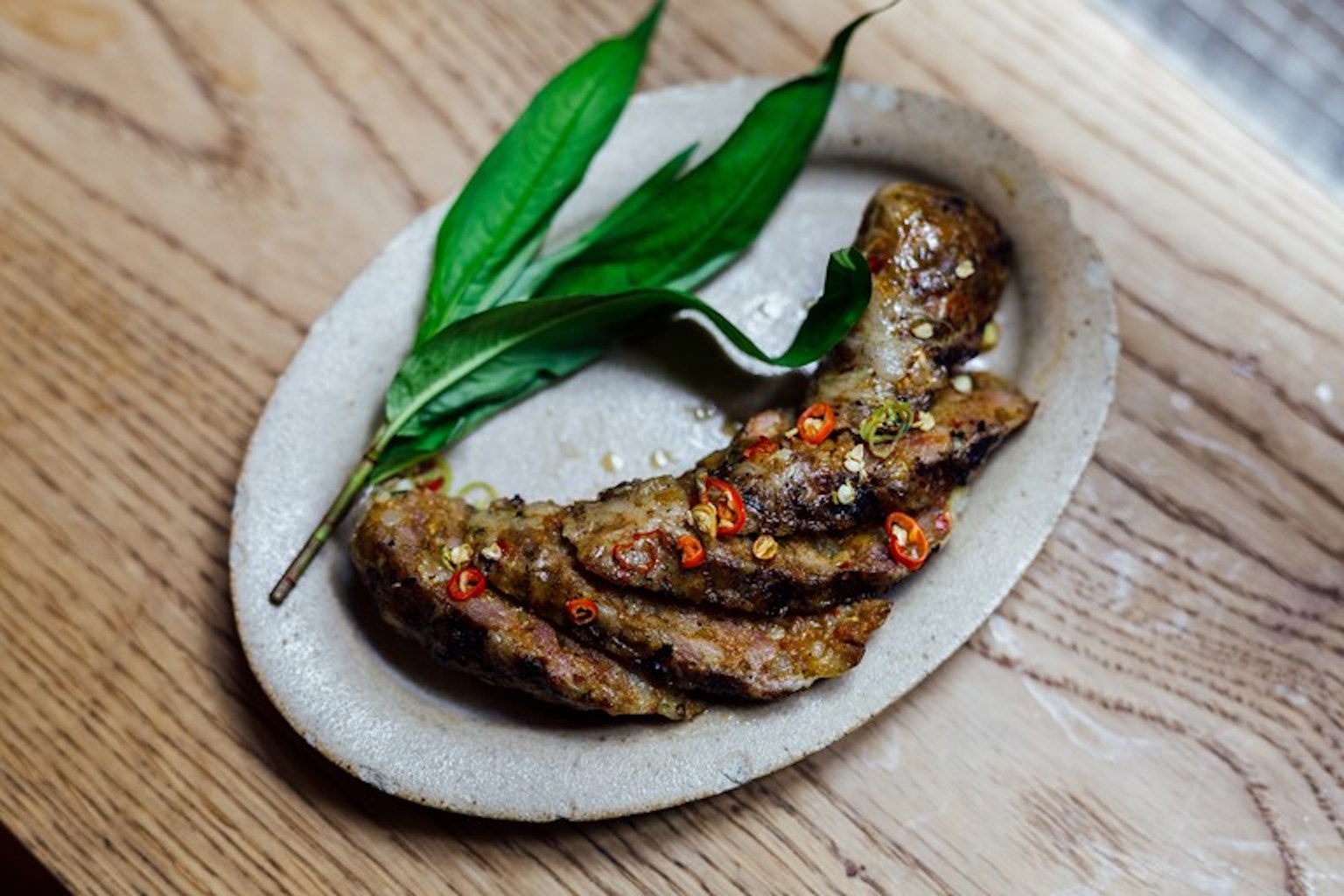 A sliced Thai sausage on a platter scattered with chilli