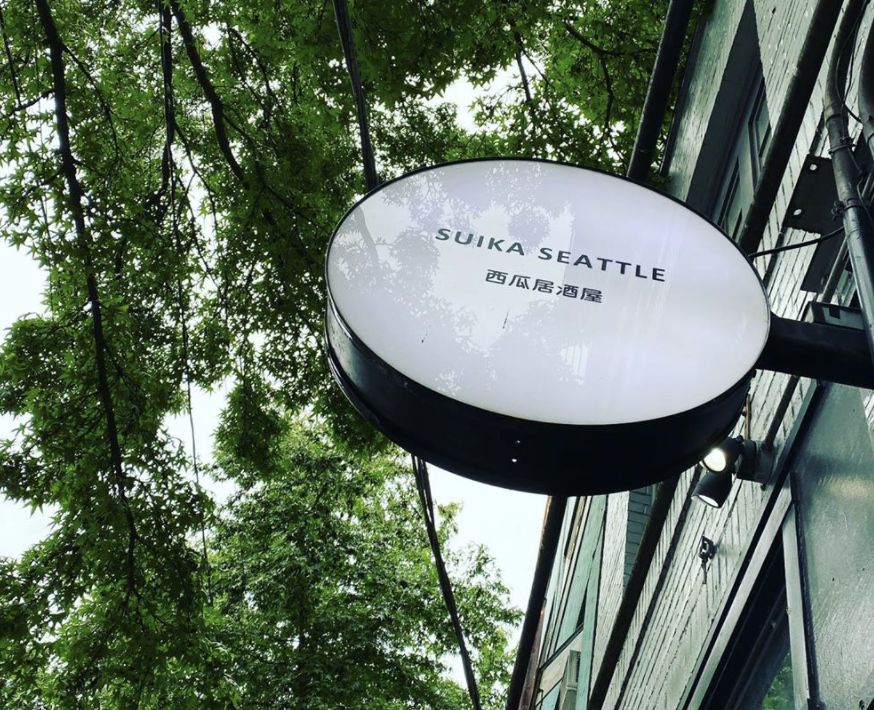 The round sign outside Suika in Seattle, with Japanese letter (and Suika’s name in English) against a backdrop of leafy green trees