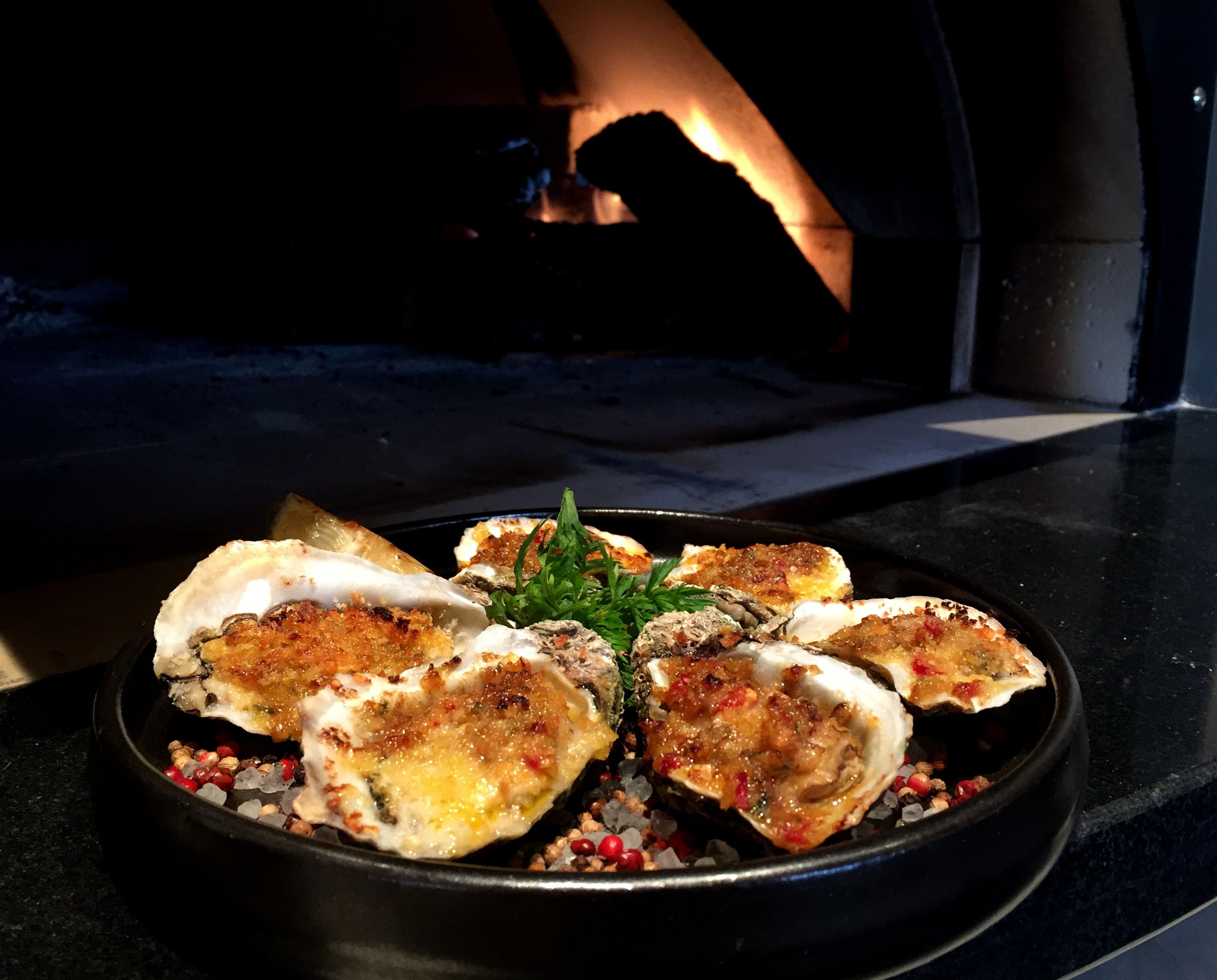 six chargrilled oysters on a plate with a large fireplace in the background