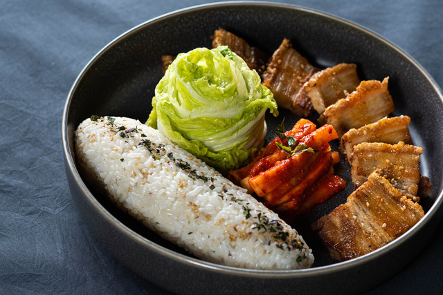 A view of Korean pork belly, with cabbage and a cylinder of seasoned rice on the side