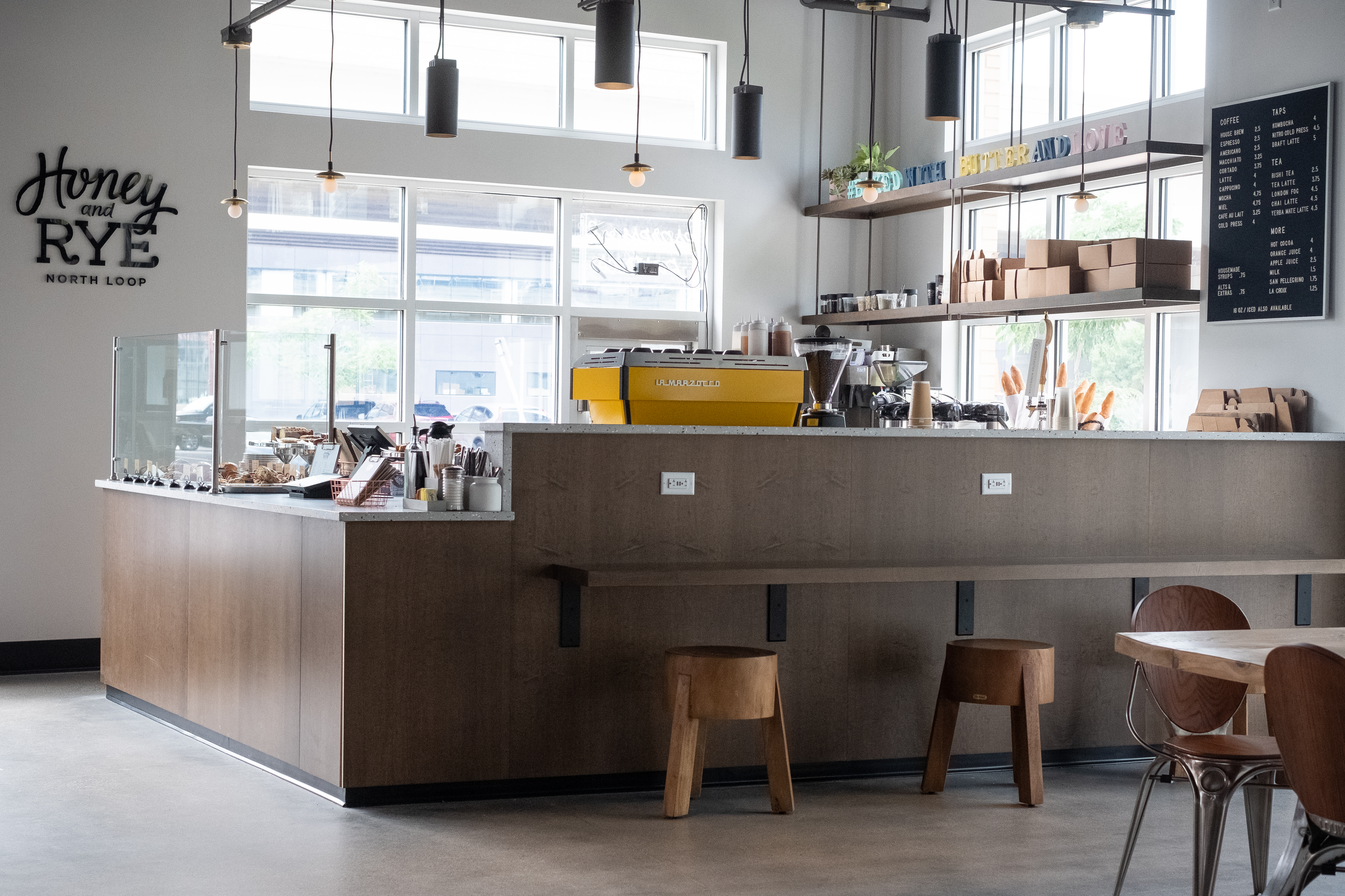 The view of Honey &amp; Rye with a bar alongside it, a counter, and bright yellow espresso machine