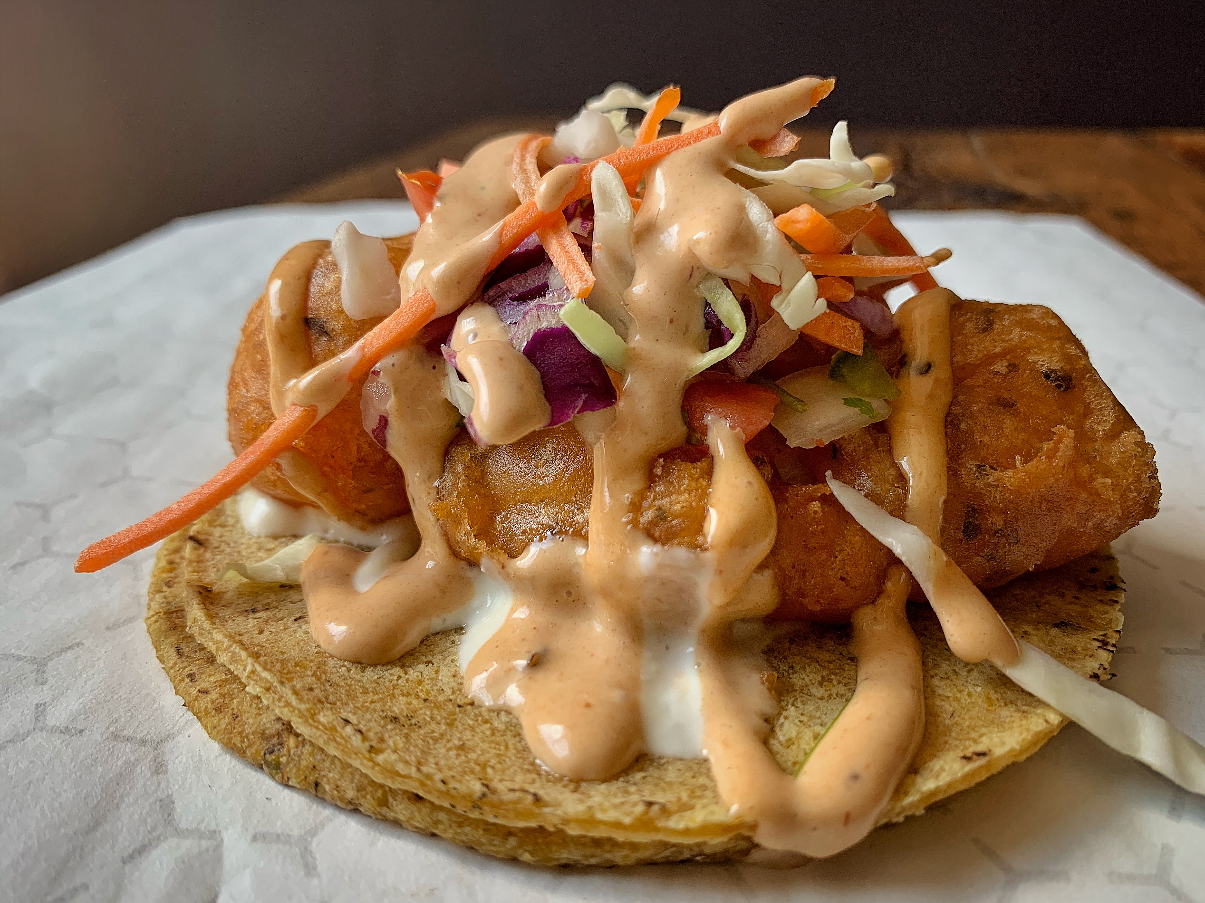 Closeup of a taco with fried fish, slaw, crema, and a drizzle of a creamy orange sauce