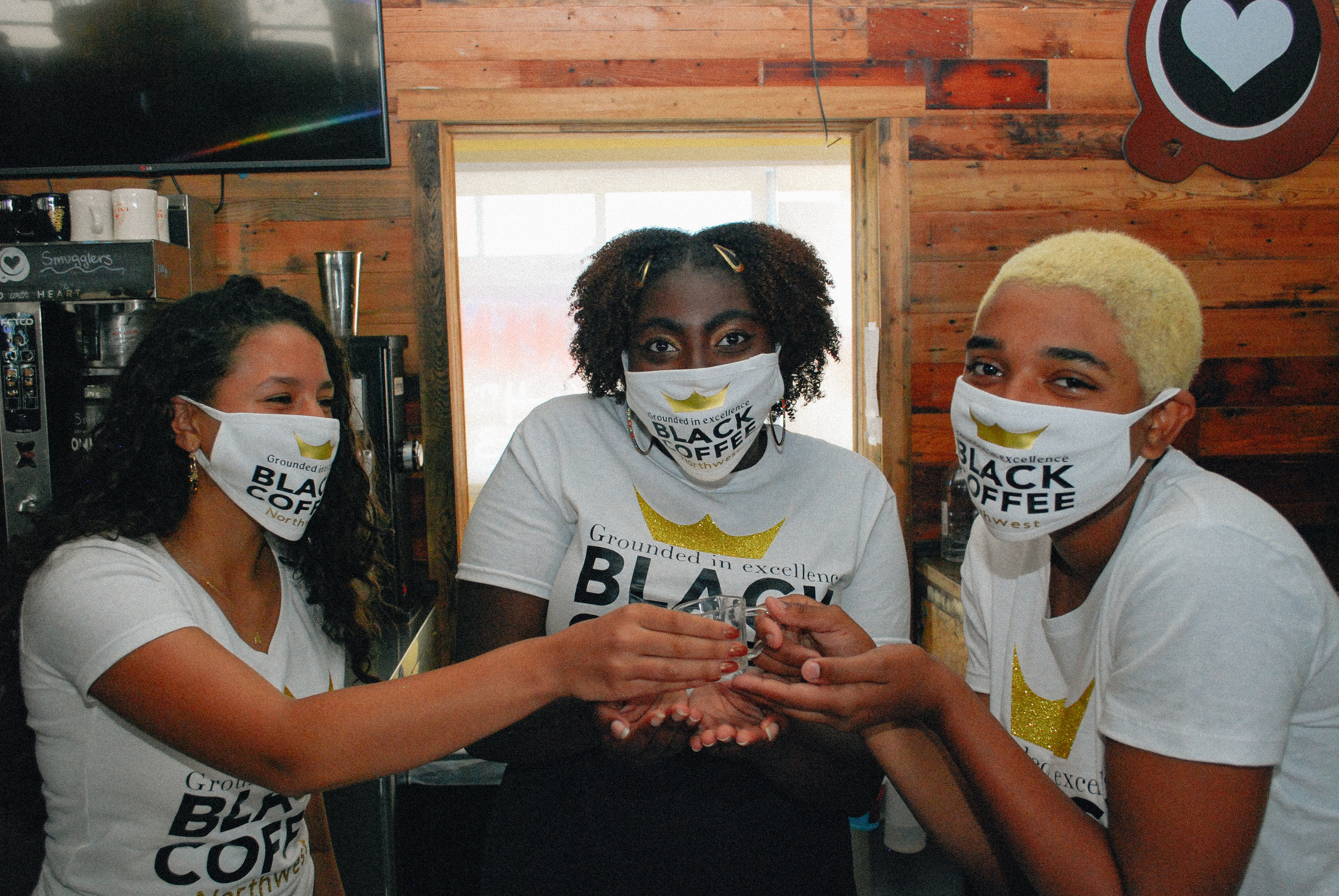 Three young baristas wearing face masks hold up a glass at Black Coffee Northwest in Shoreline.
