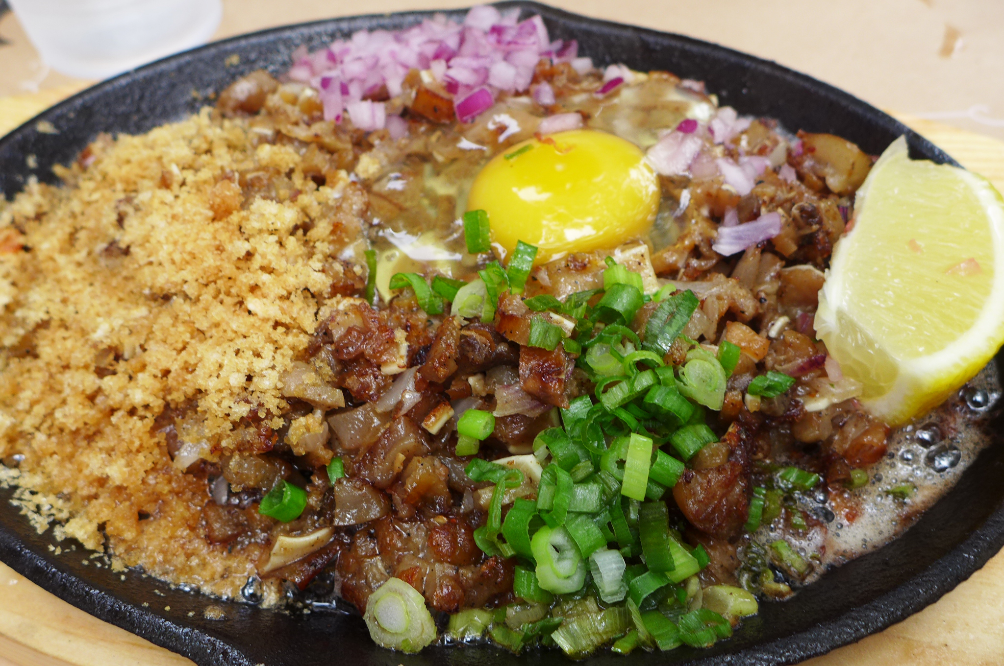 A black metal platter with minced pork parts and skin, plus a raw egg cracked on top.
