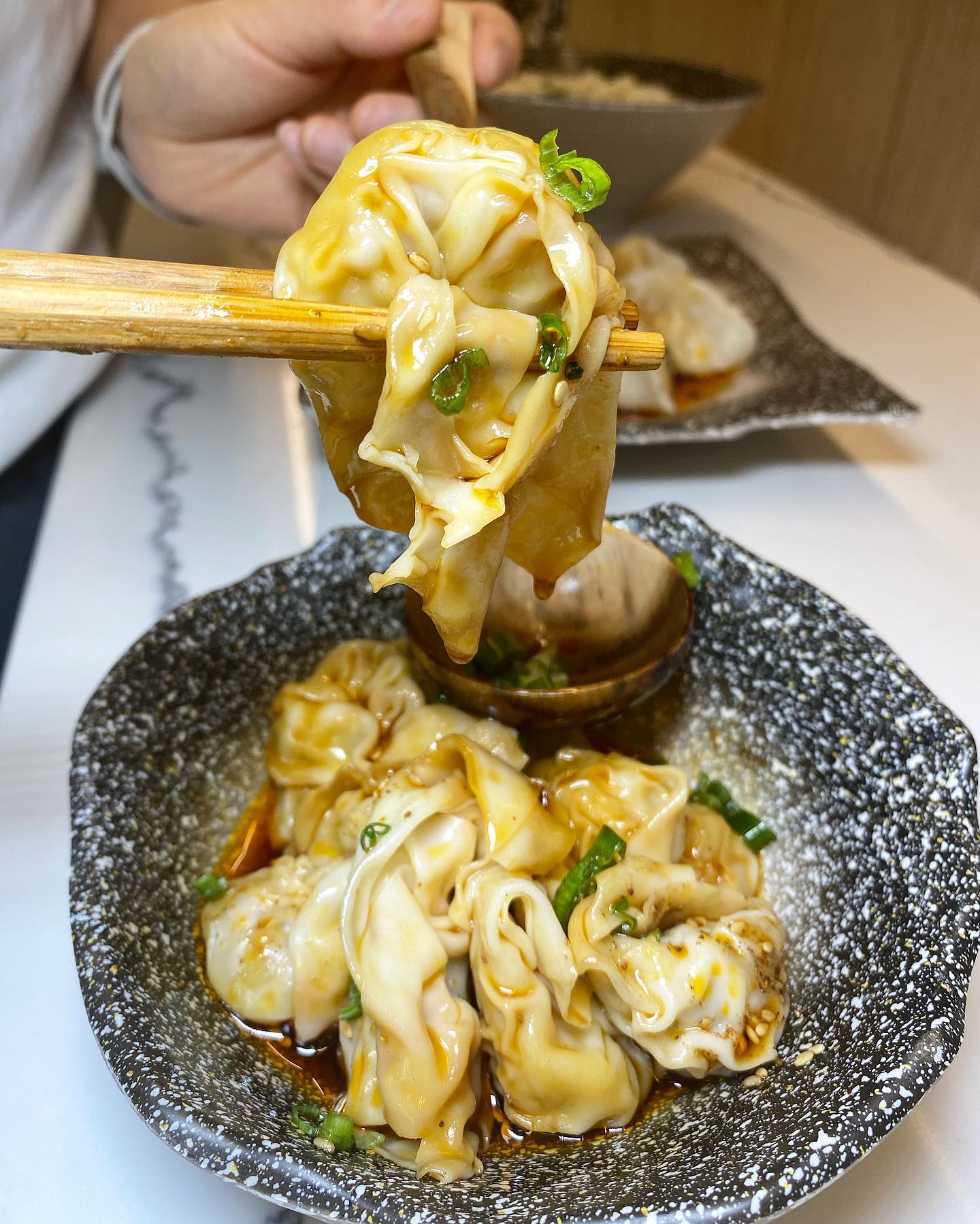 A pair of chopsticks hold a wonton over a bowl of wontons