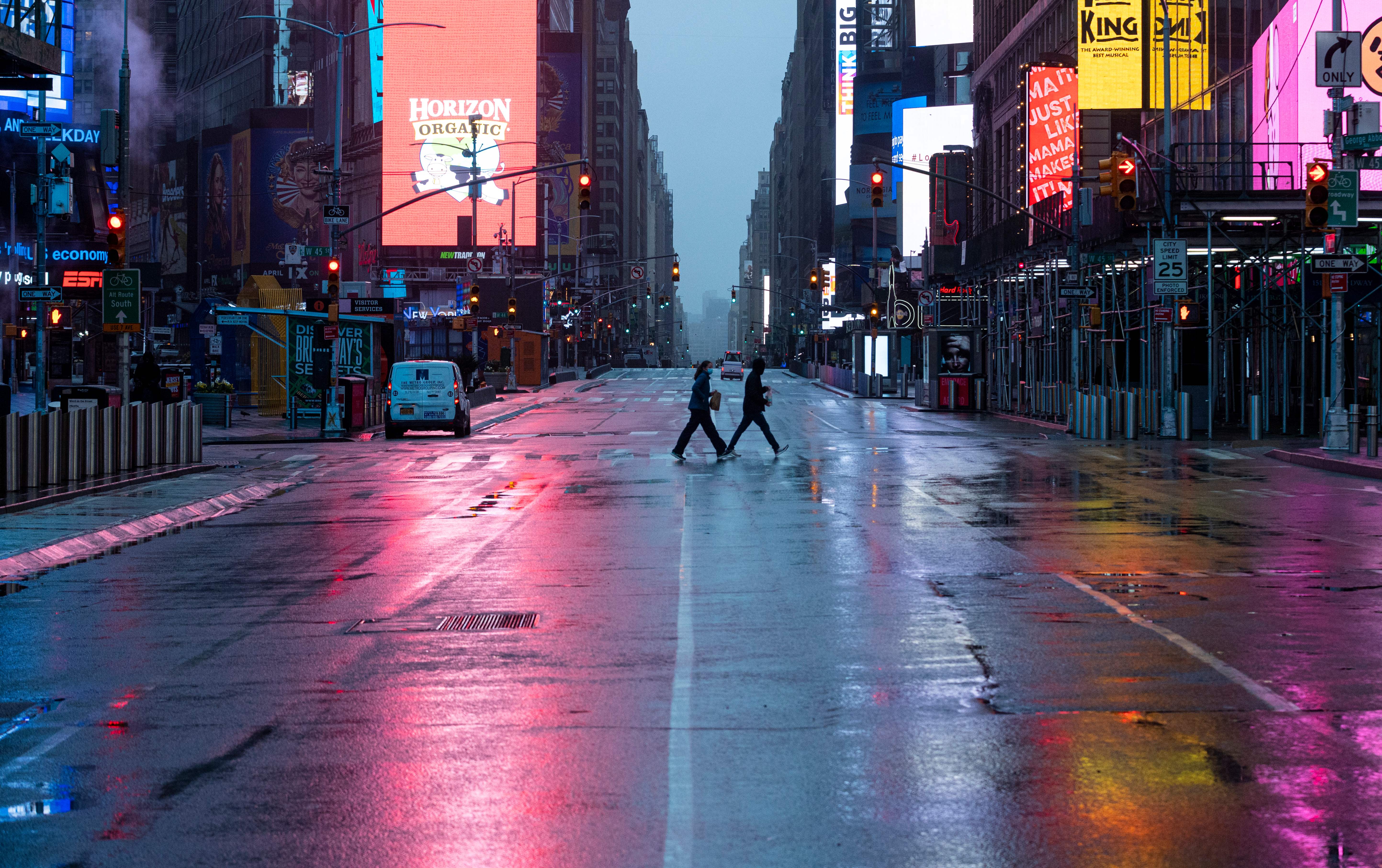 A couple walking across Times Square at dusk.