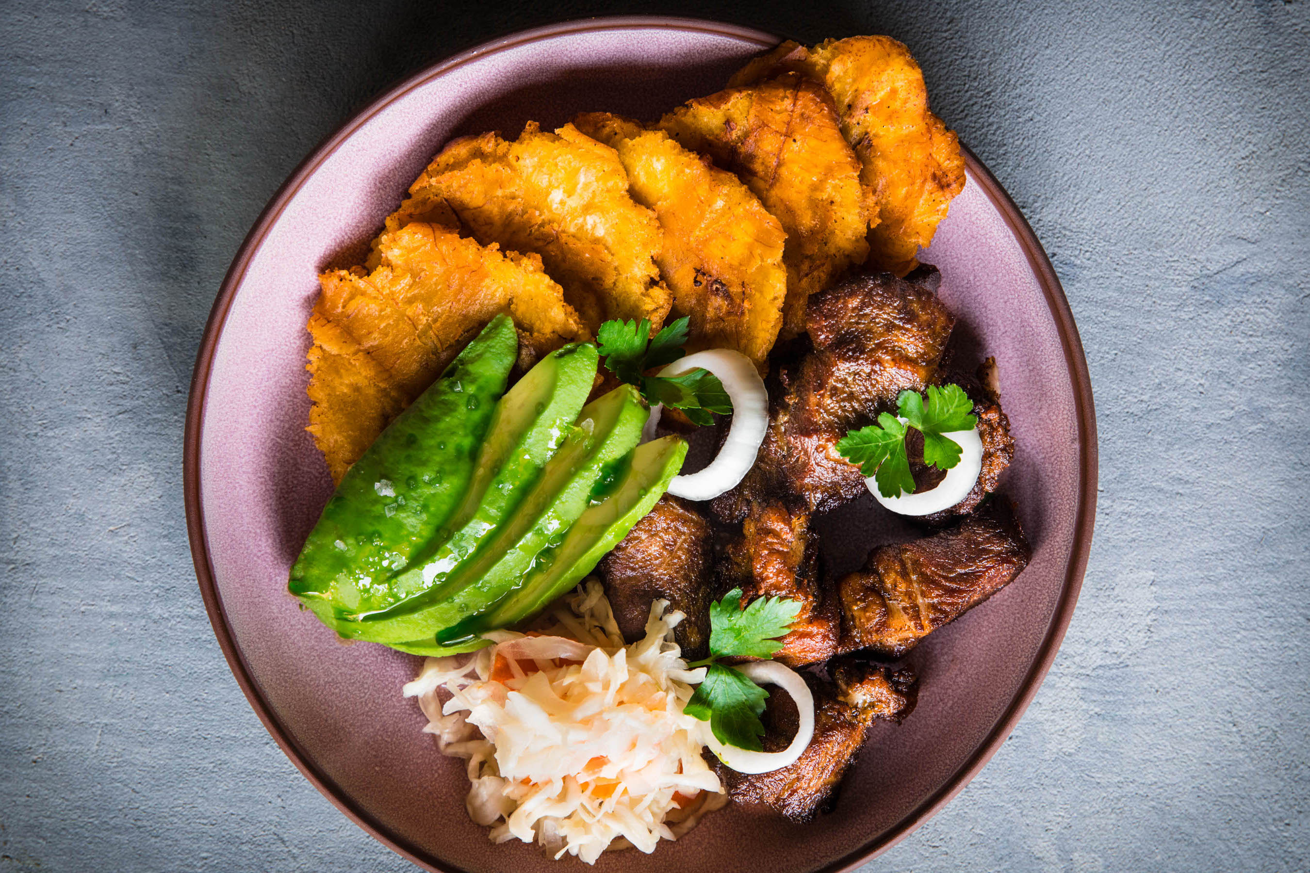 Fried plantains, avocado, pikliz, and more on a plate from Kann.
