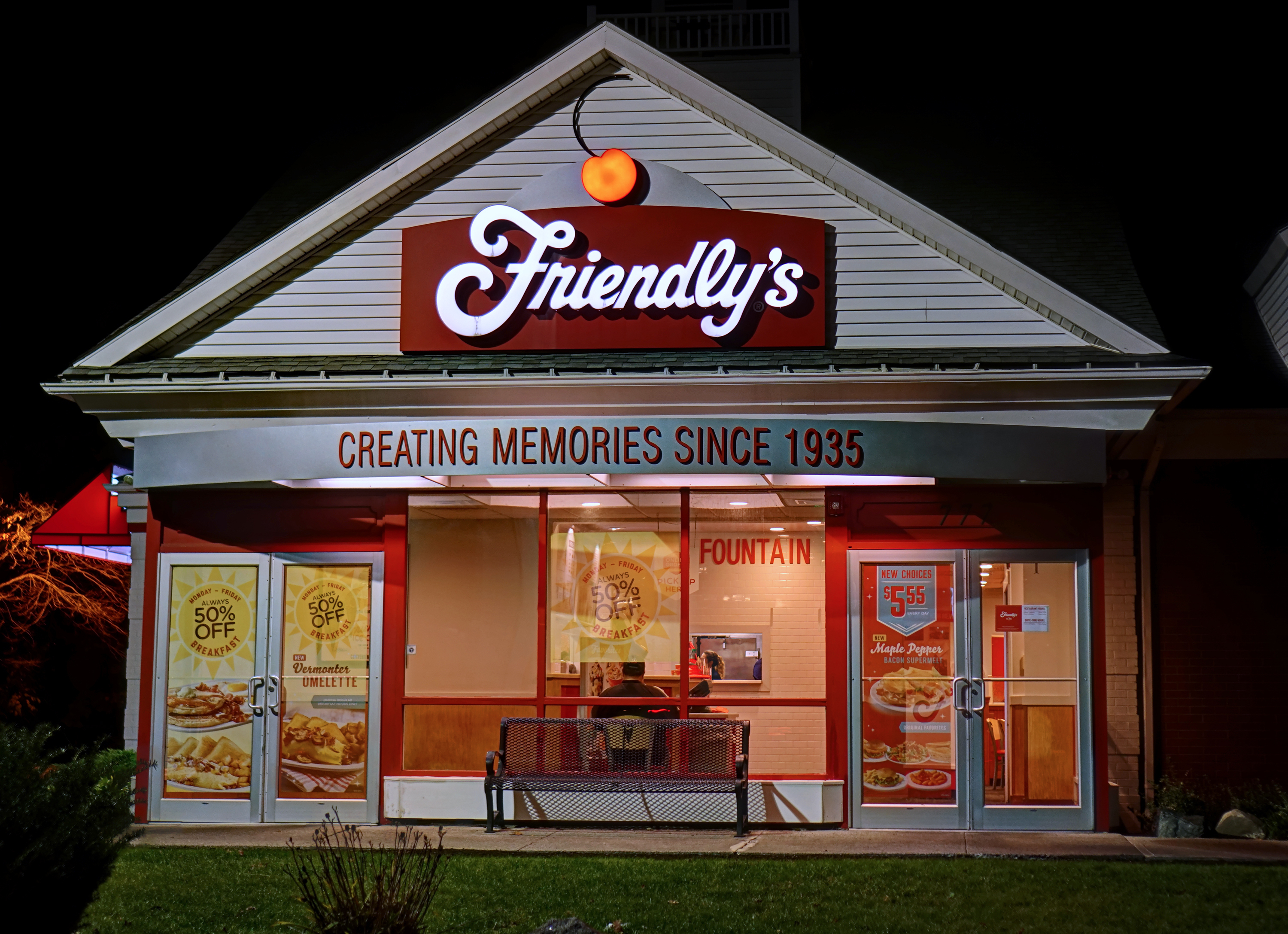 The exterior of a Friendly’s restaurant, lit up inside during nighttime.