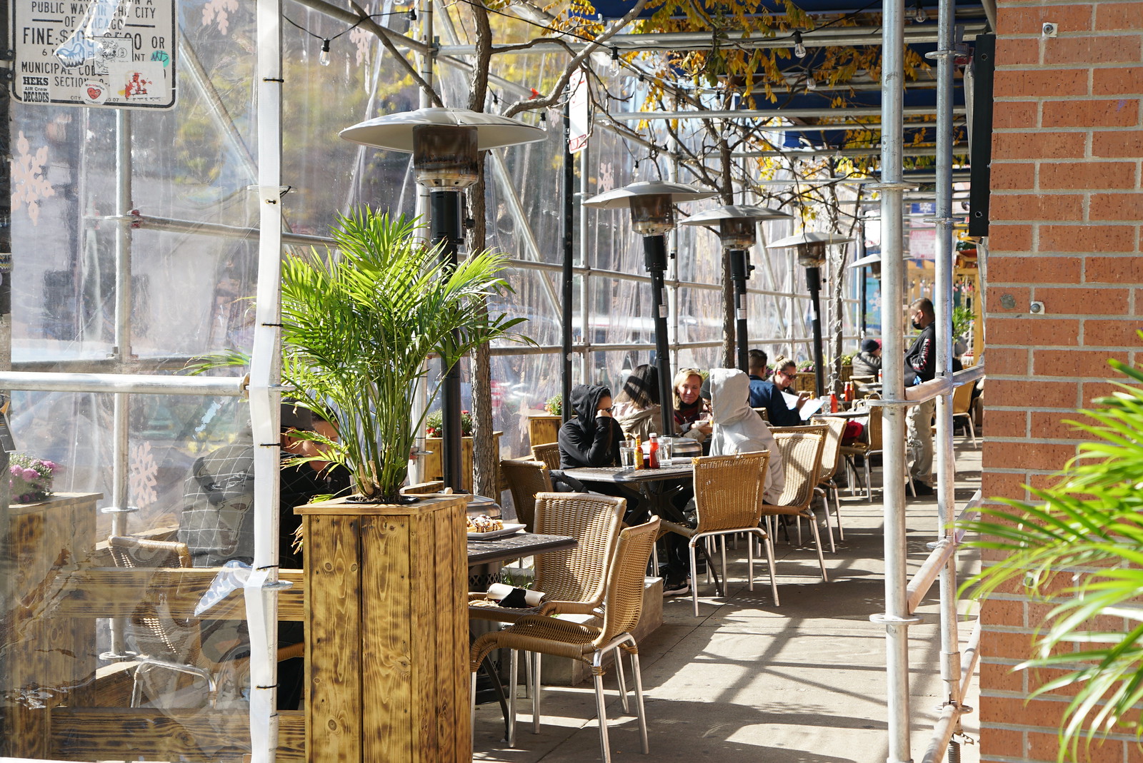 An outdoor dining area with heaters and people sitting at tables that’s covered.
