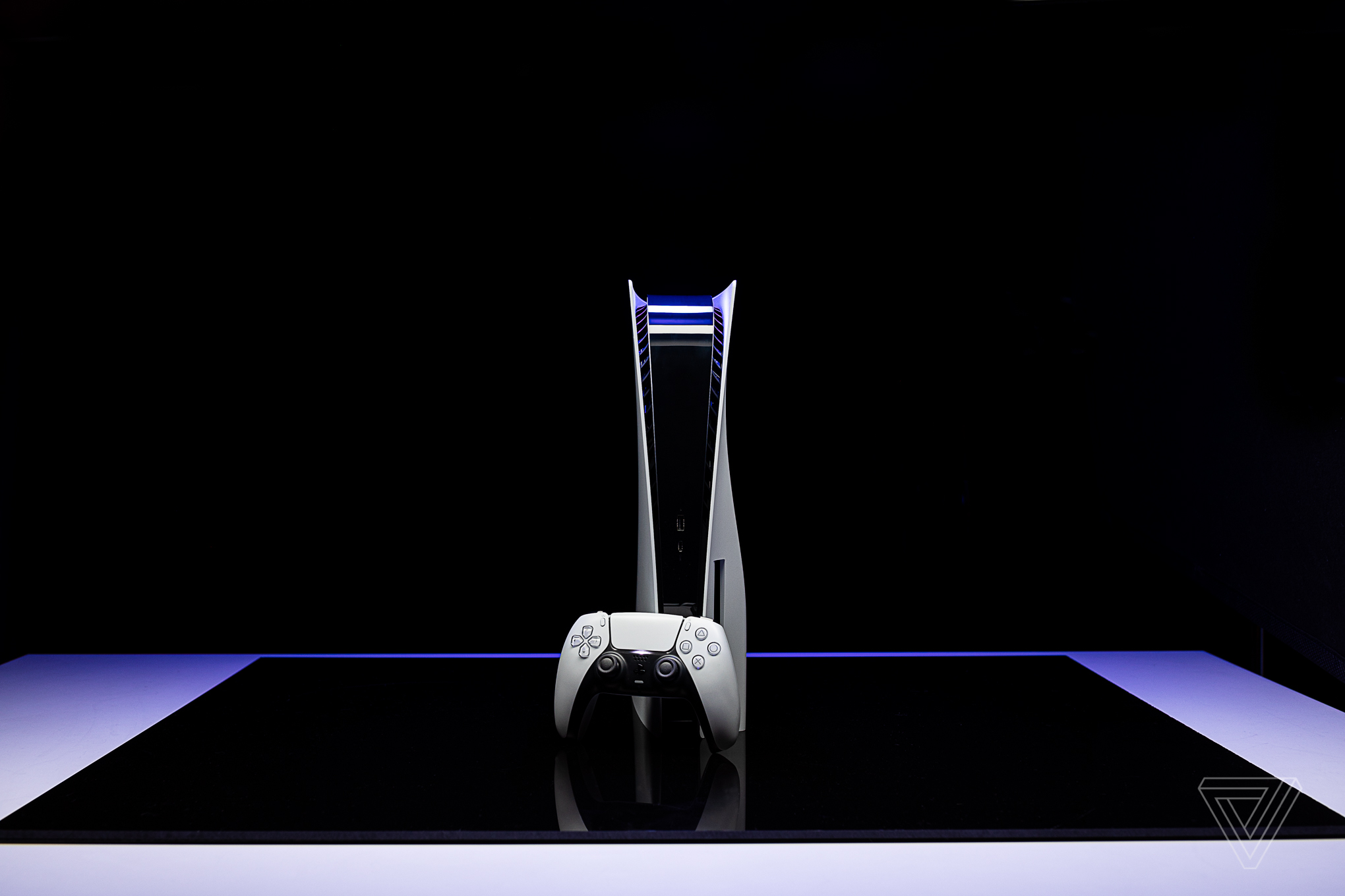 A studio shot of the PlayStation 5 standing vertically with an upright DualSense controller in front of it, against a black background.
