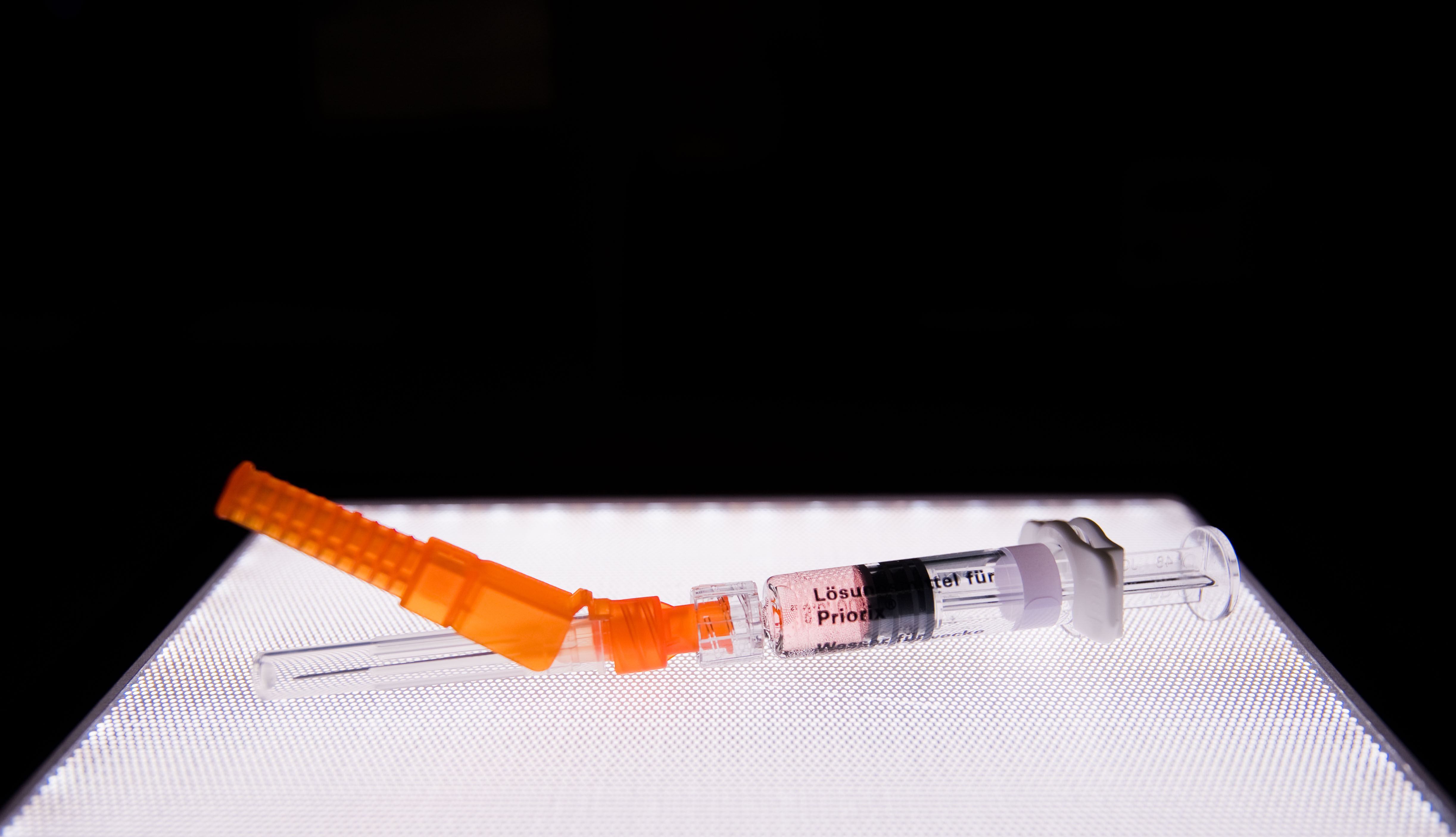 A vaccination syringe sitting on a lit square.
