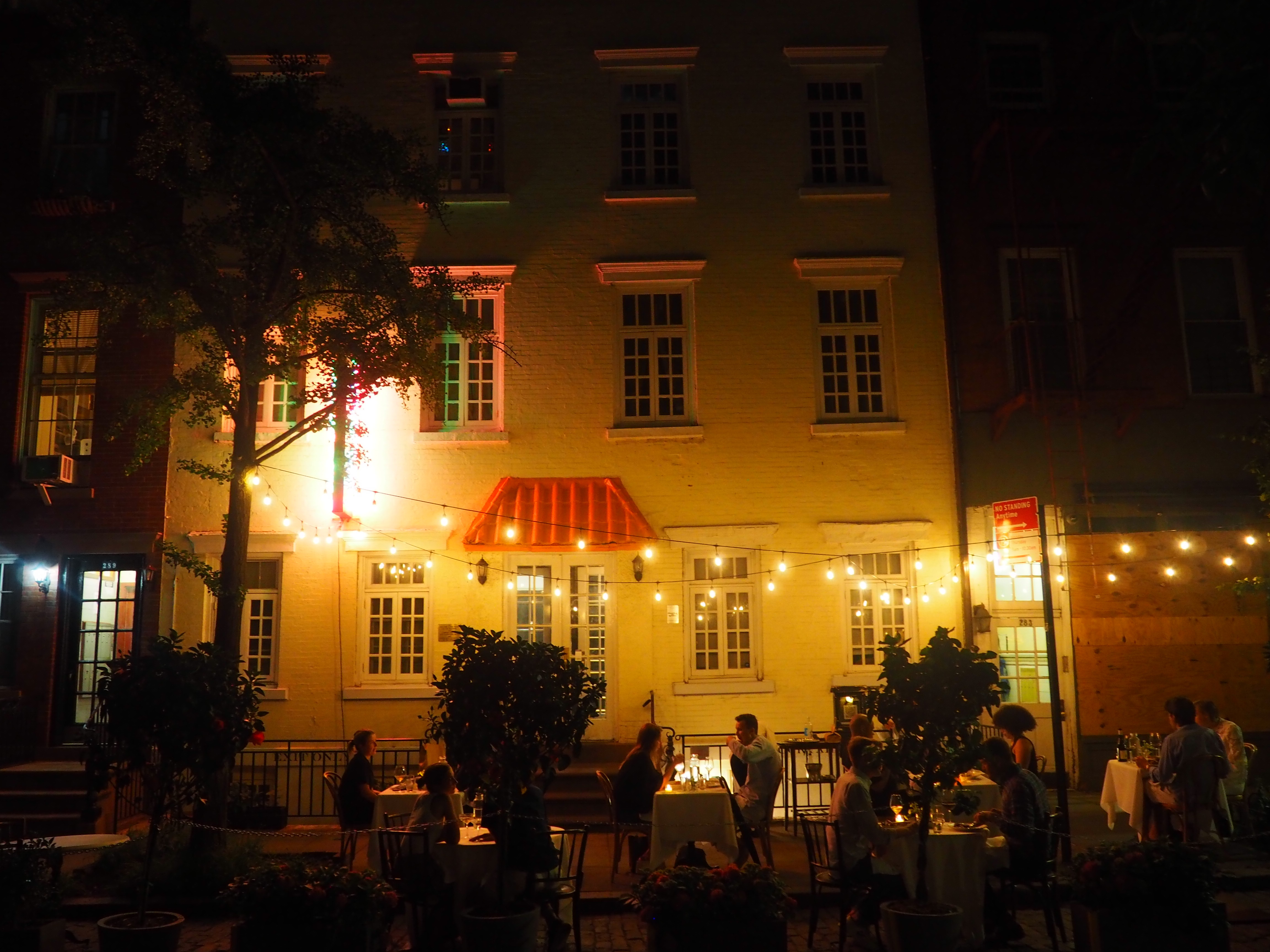 Outdoor dining in front of a restaurant at night with lights strung up around the outdoor tables