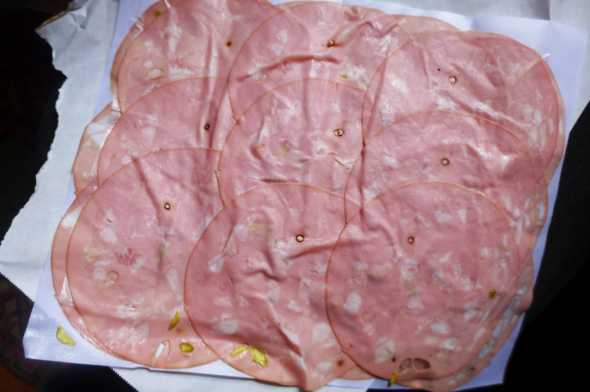Thin overlapping slices of mortadella on a white butcher paper.