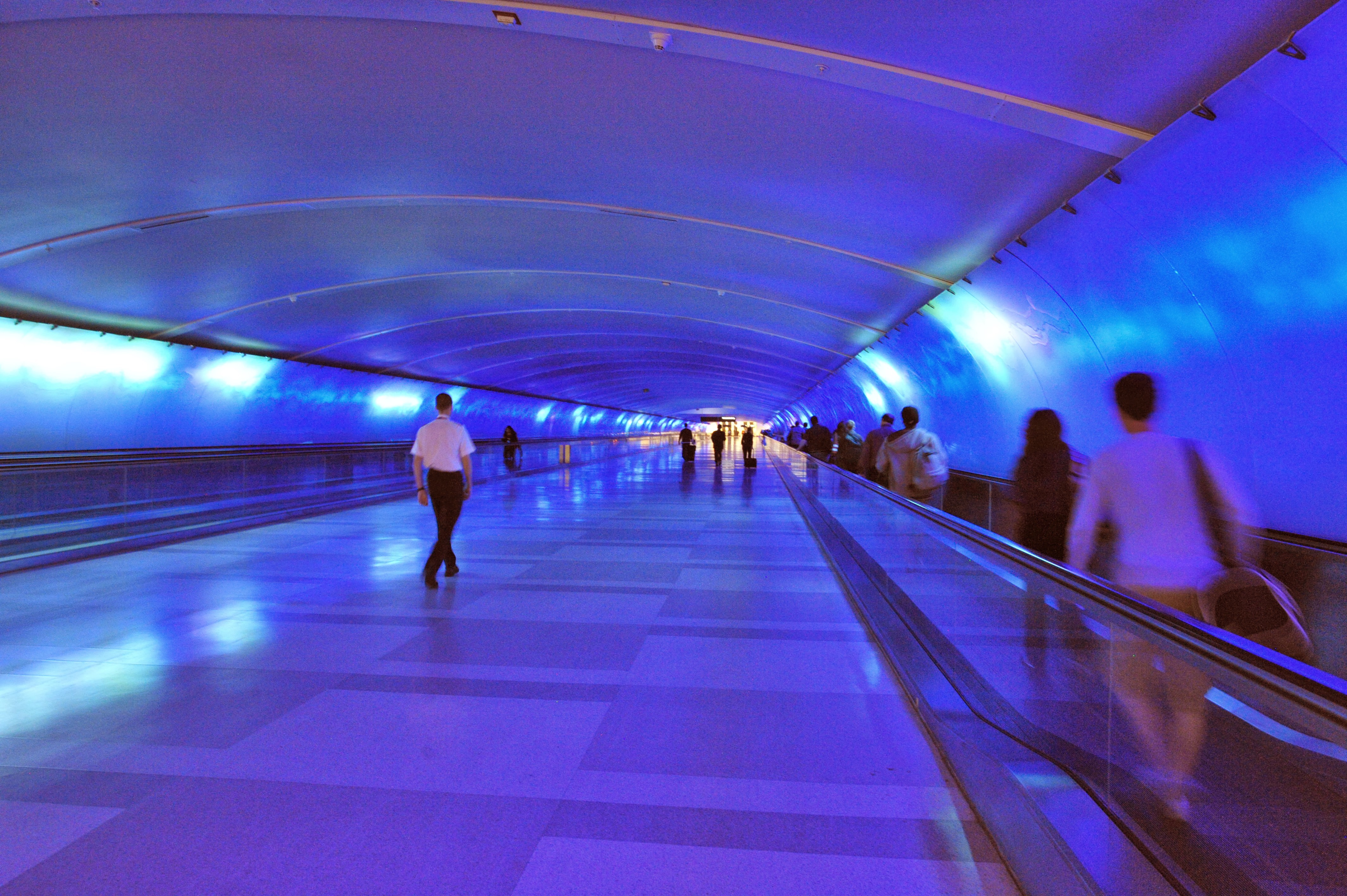 People pass through a tunnel at DTW that’s filled with purple light.