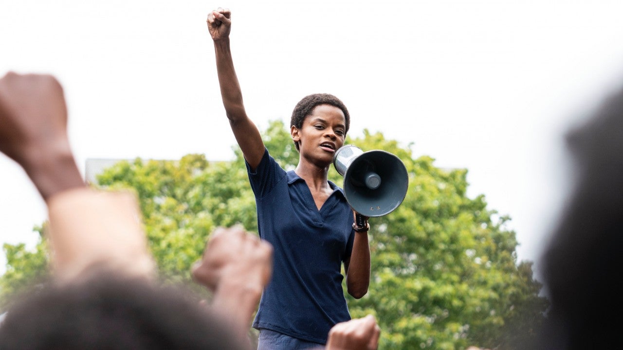 A woman stands with a raised fist and a megaphone.