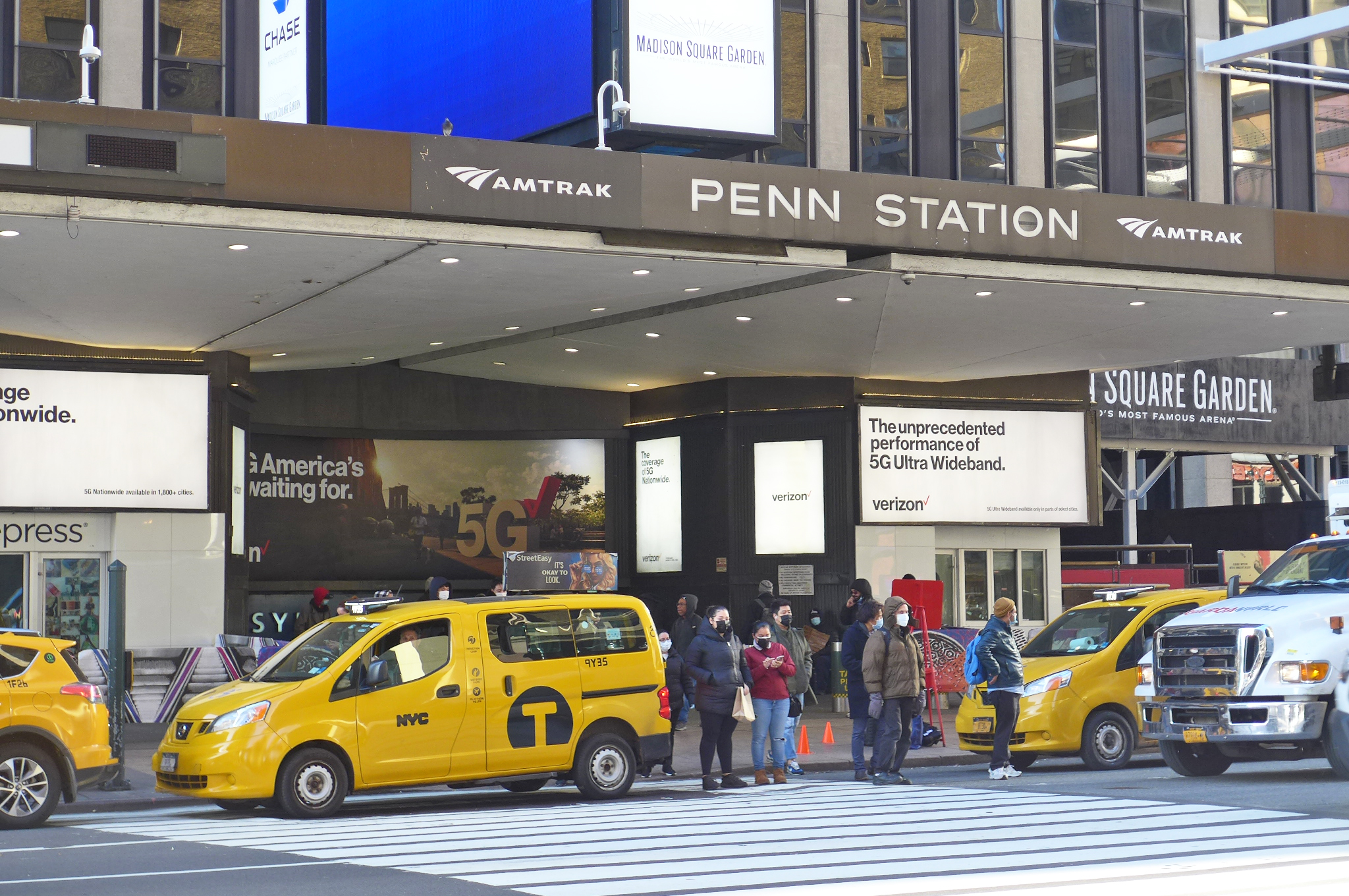 Cabs double parked outside the entrance to Penn Station with a crowd about to cross the street toward us.
