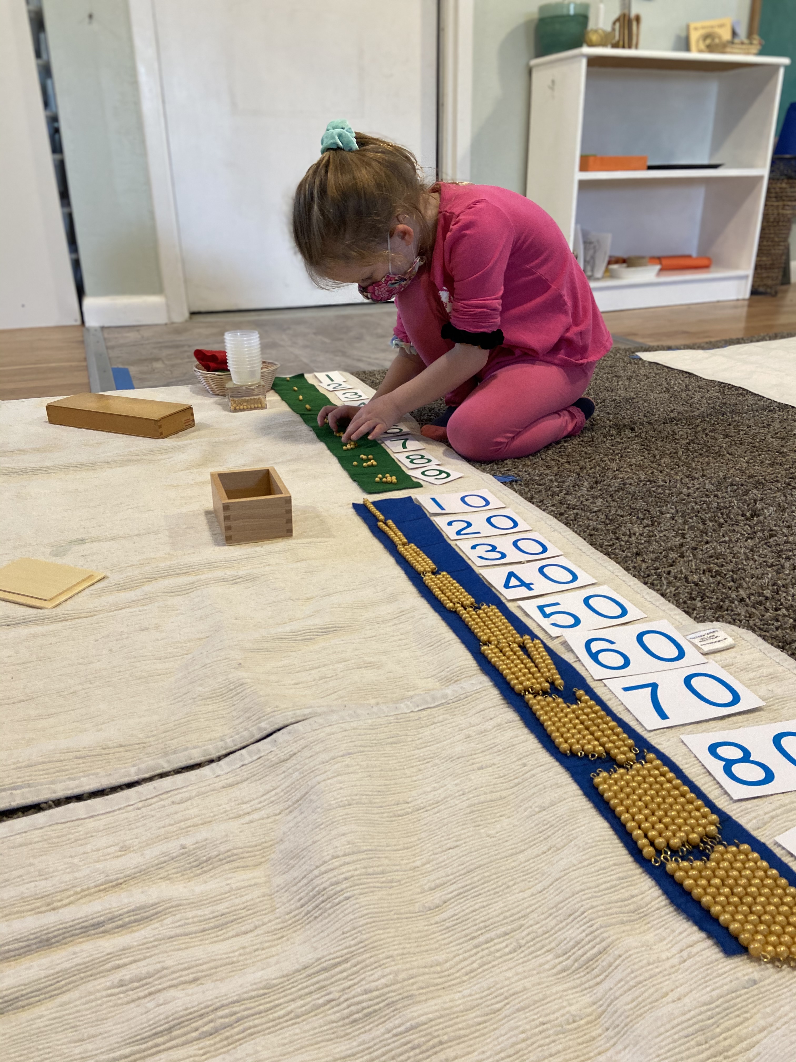 A masked young child plays with numbers and blocks.