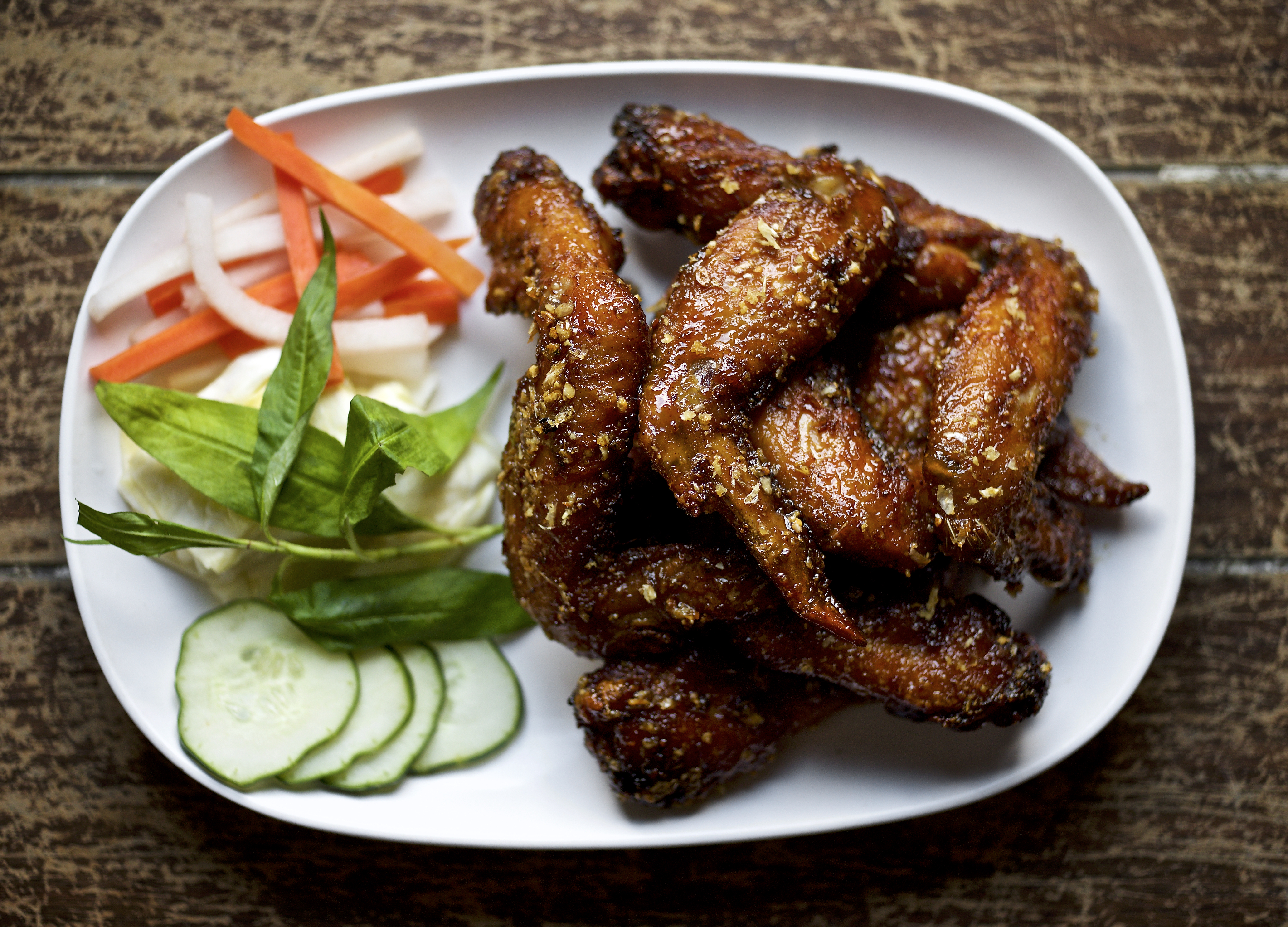 A plate of chicken wings with carrots, cucumbers, and more on the left