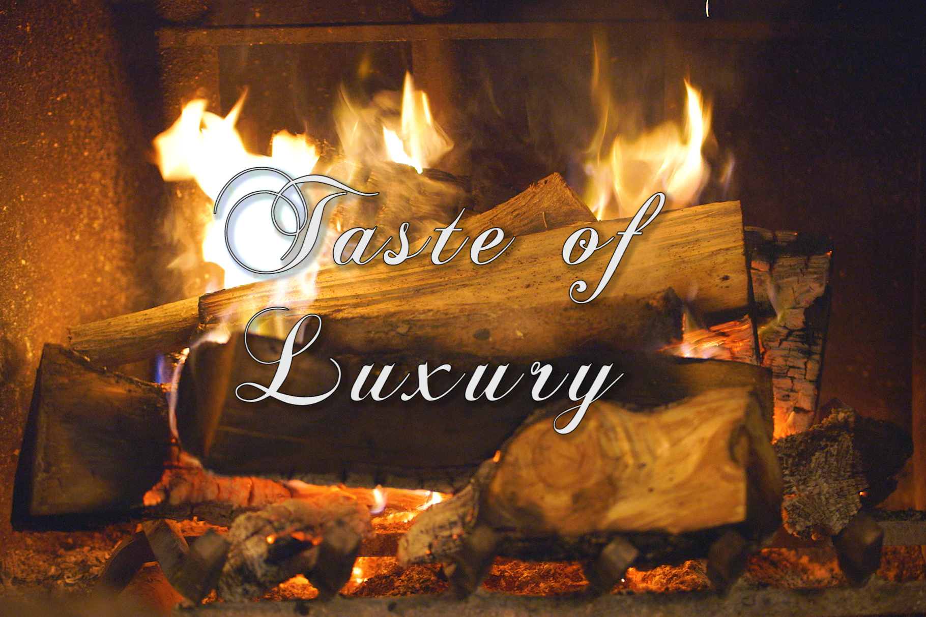 The words “Taste of Luxury” in white script front superimposed over a close-up photo of a wood fire burning in a fireplace.