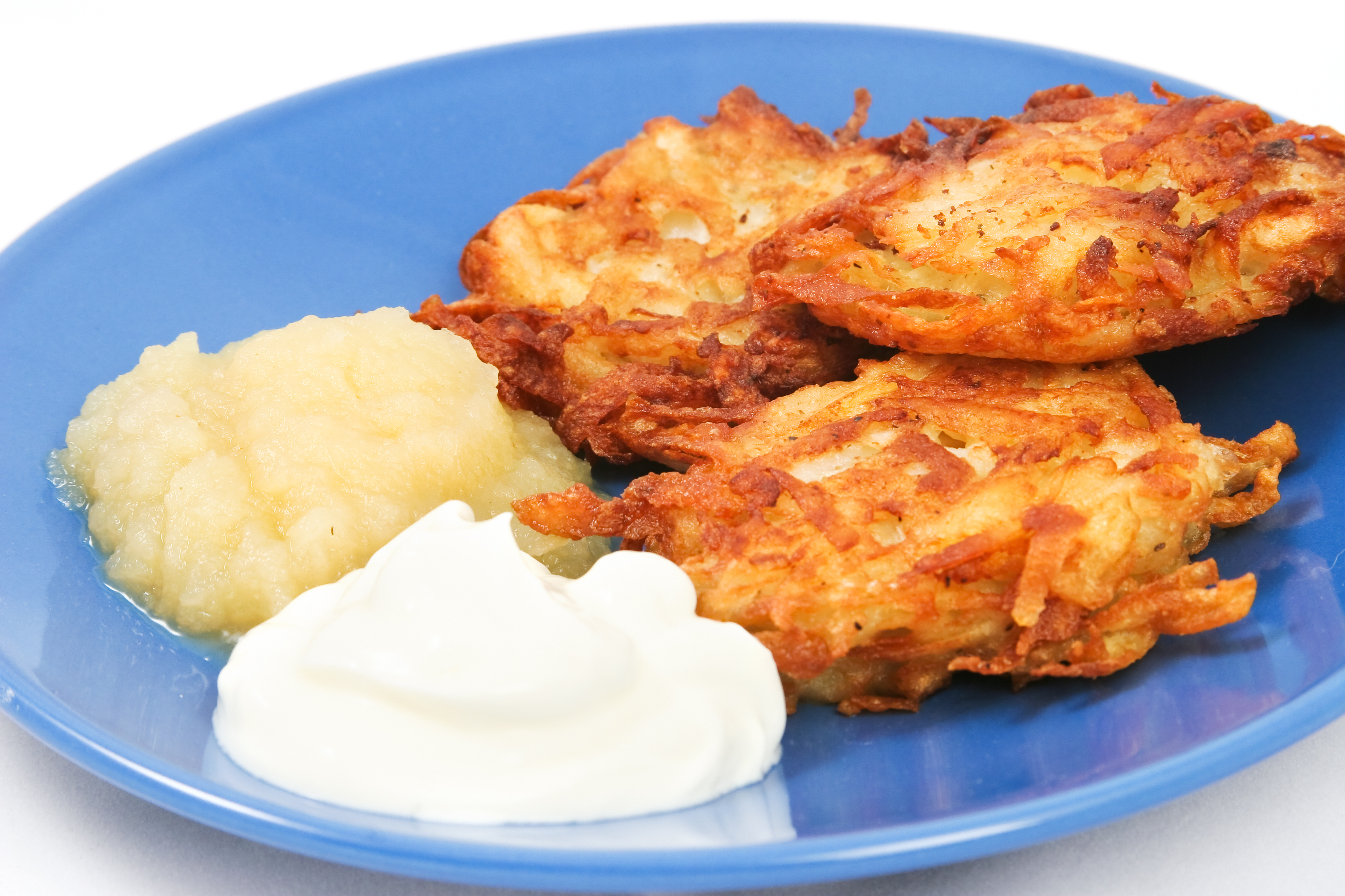 Latkes with apple sauce and sour cream on a blue plate.