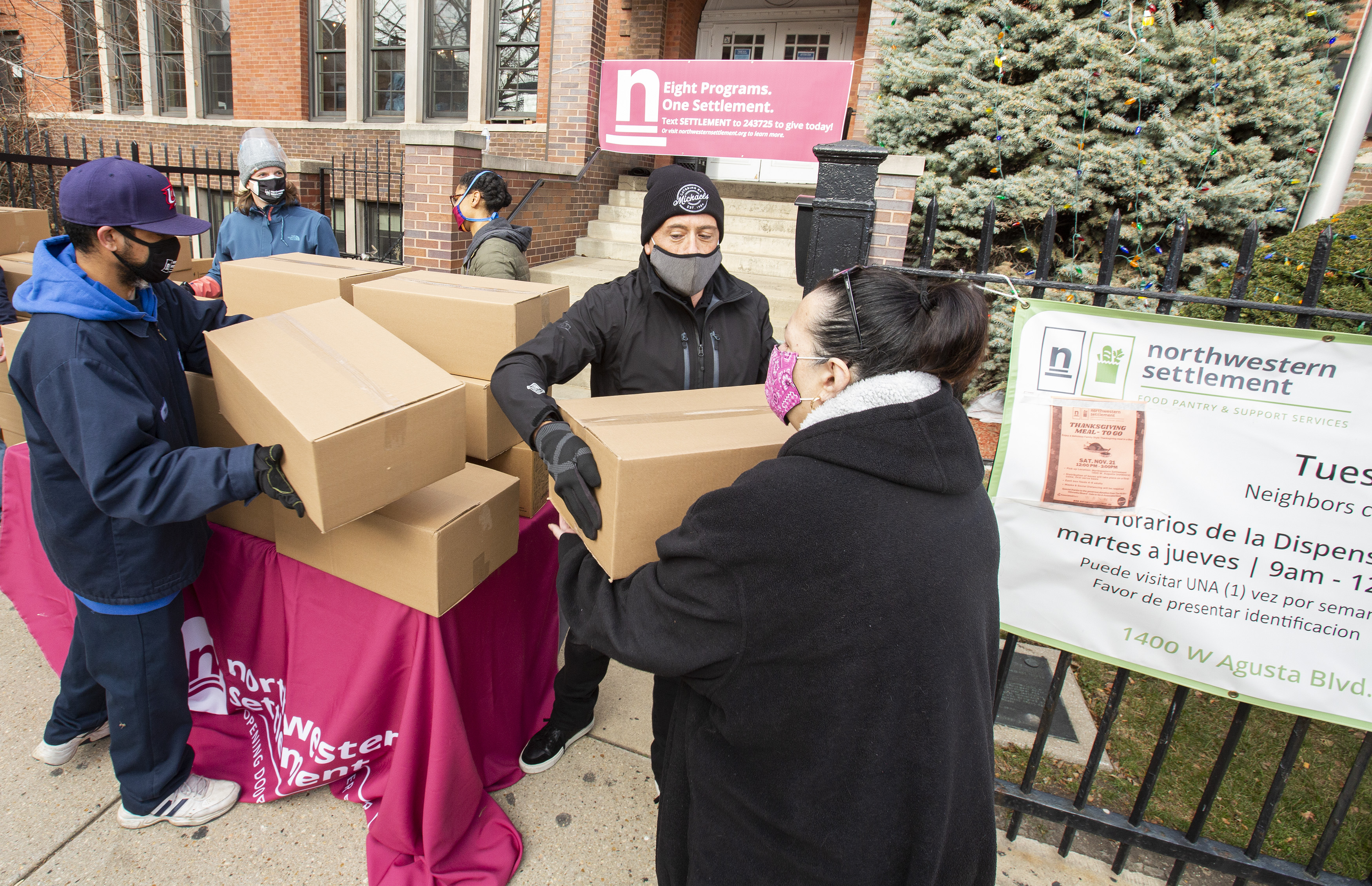 A group of people in masks hand out big boxes of  food.