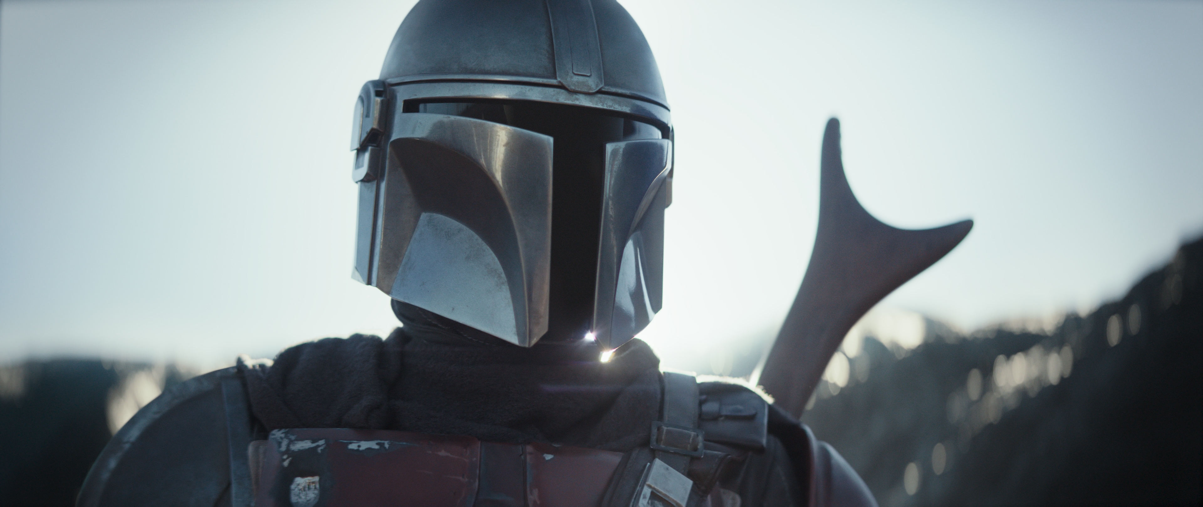 the mandalorian in tight close-up with a shiny helmet and gun sticking out of frame
