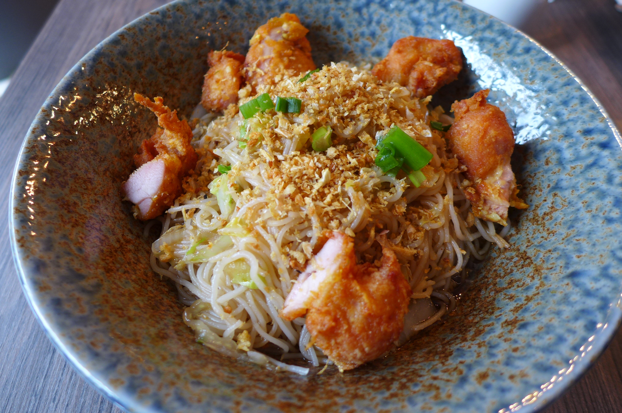 A nest of noodles with crunchy shallots and fried shrimp on top.