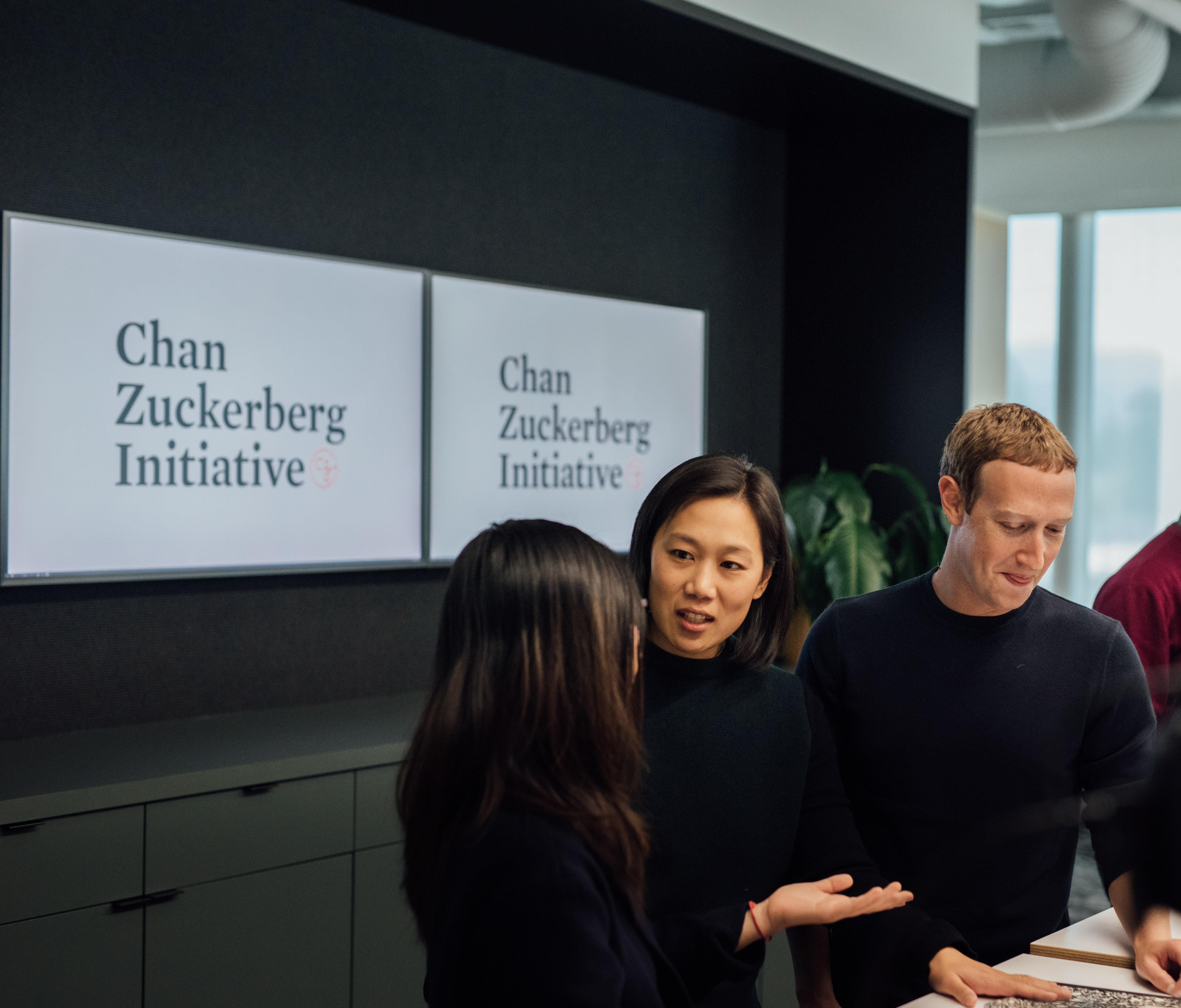 Priscilla Chan and Mark Zuckerberg speak with another person in front of a sign reading, “Chan Zuckerberg Initiative.”