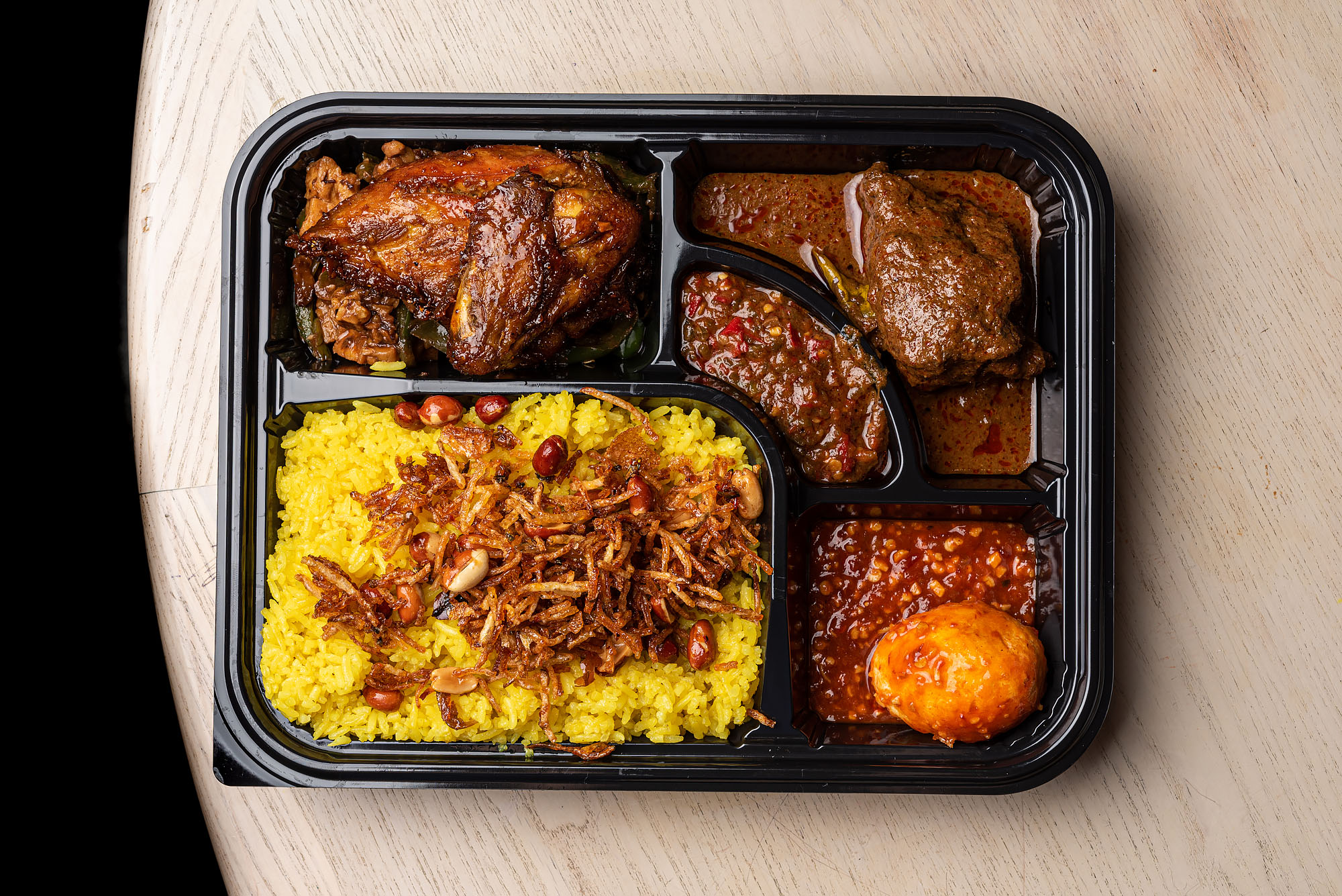 A black tray filled with Indonesian dishes and turmeric rice.