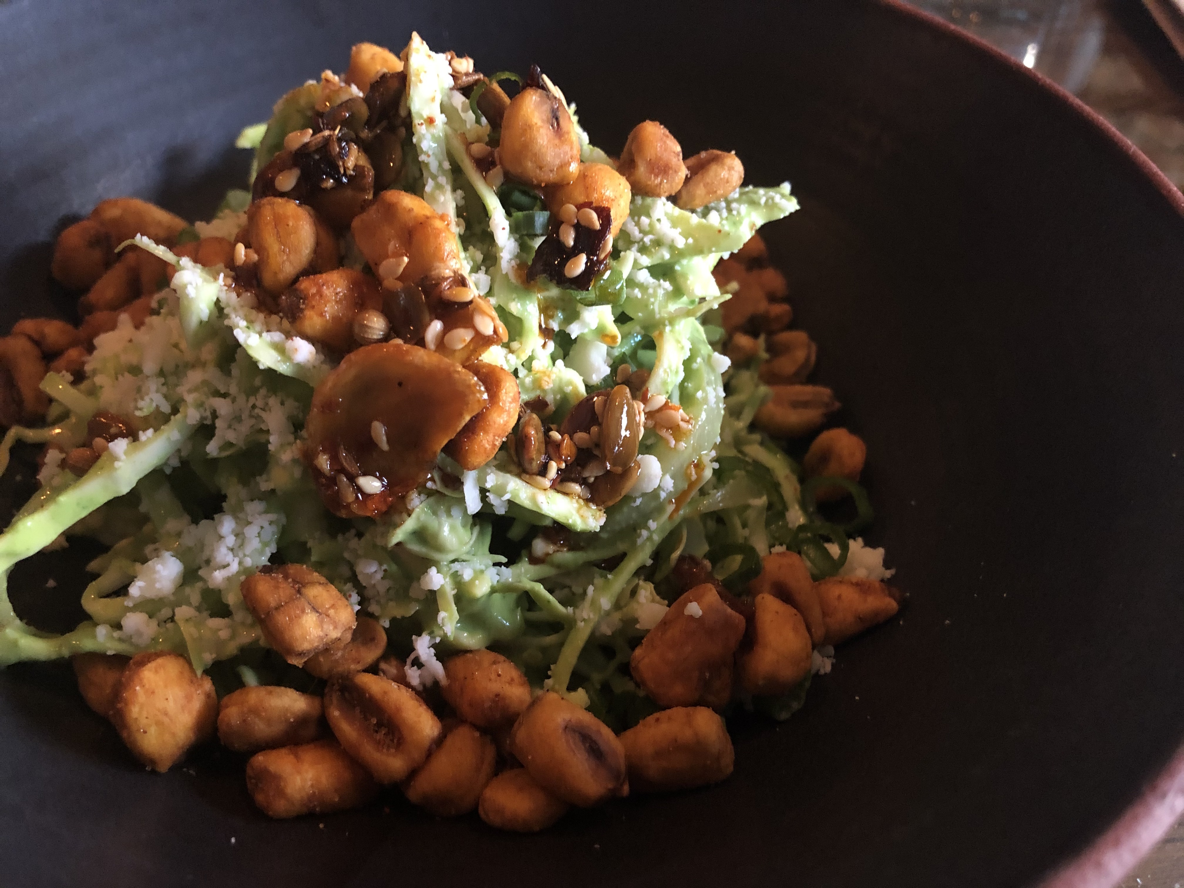 A bowl of cabbage comes topped with corn nuts and shaved cheese